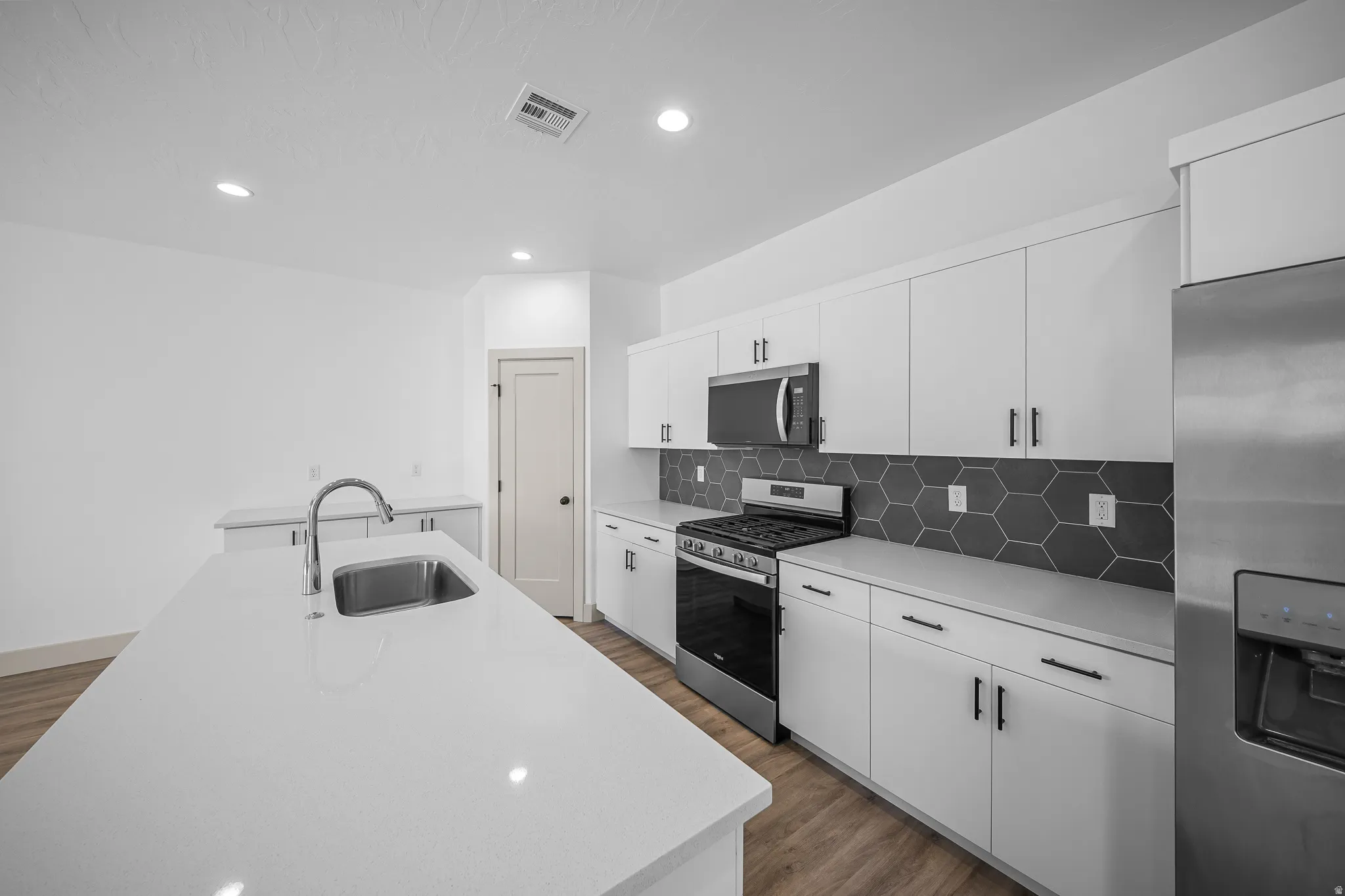 Kitchen with stainless steel appliances, white cabinets, dark wood-style floors, and recessed lighting