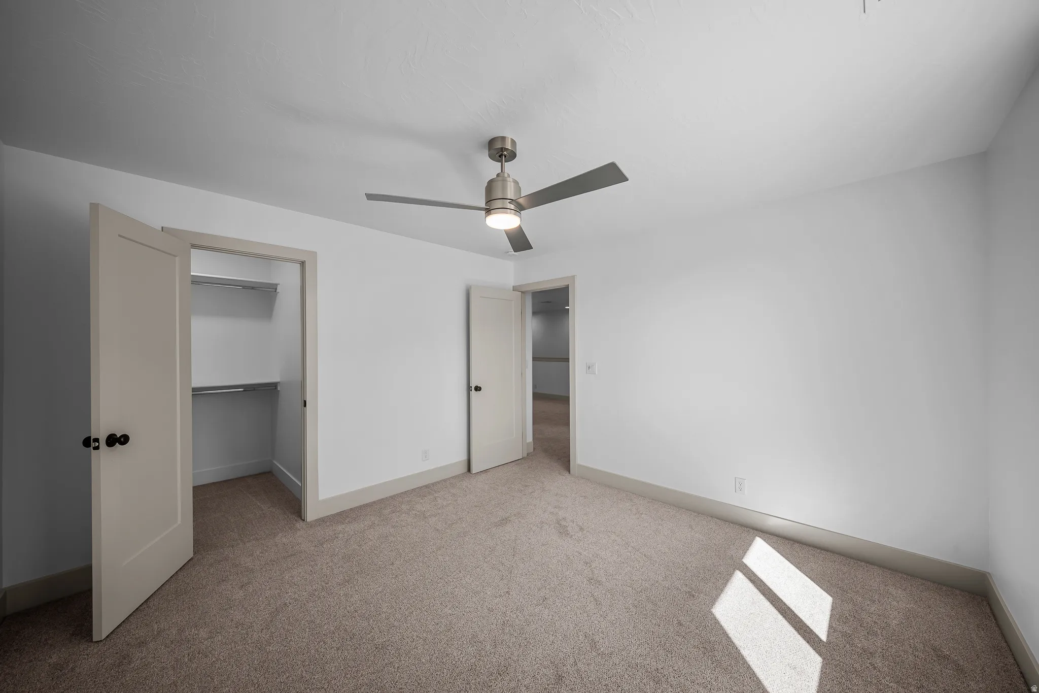 Unfurnished bedroom featuring light carpet, a spacious closet, and a ceiling fan
