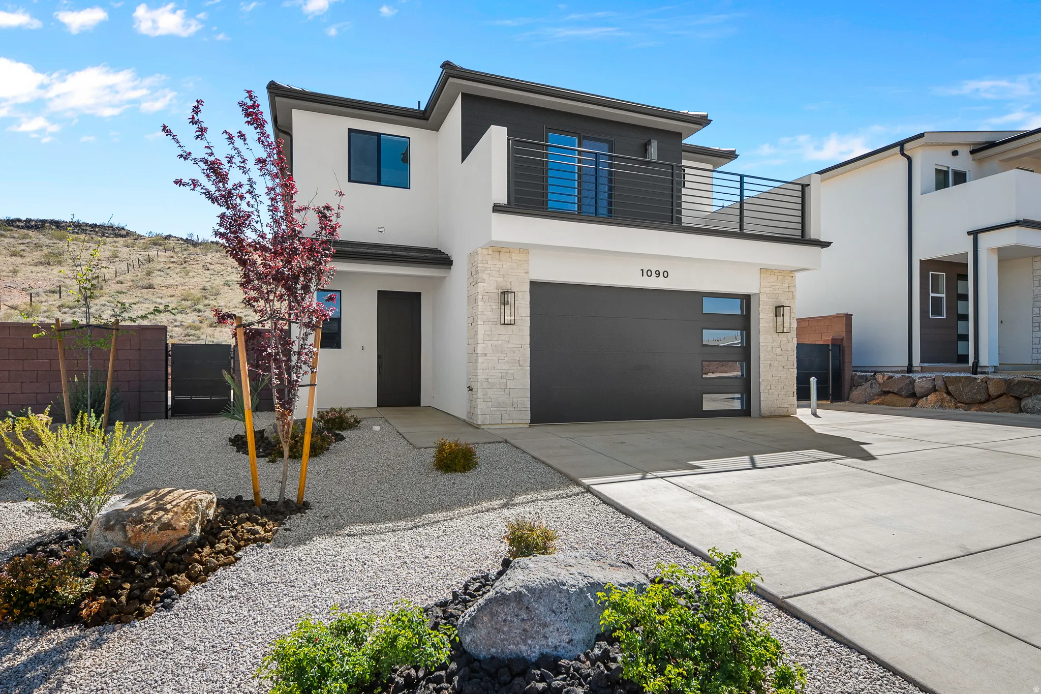 Modern home with concrete driveway, stucco siding, a balcony, an attached garage, and stone siding