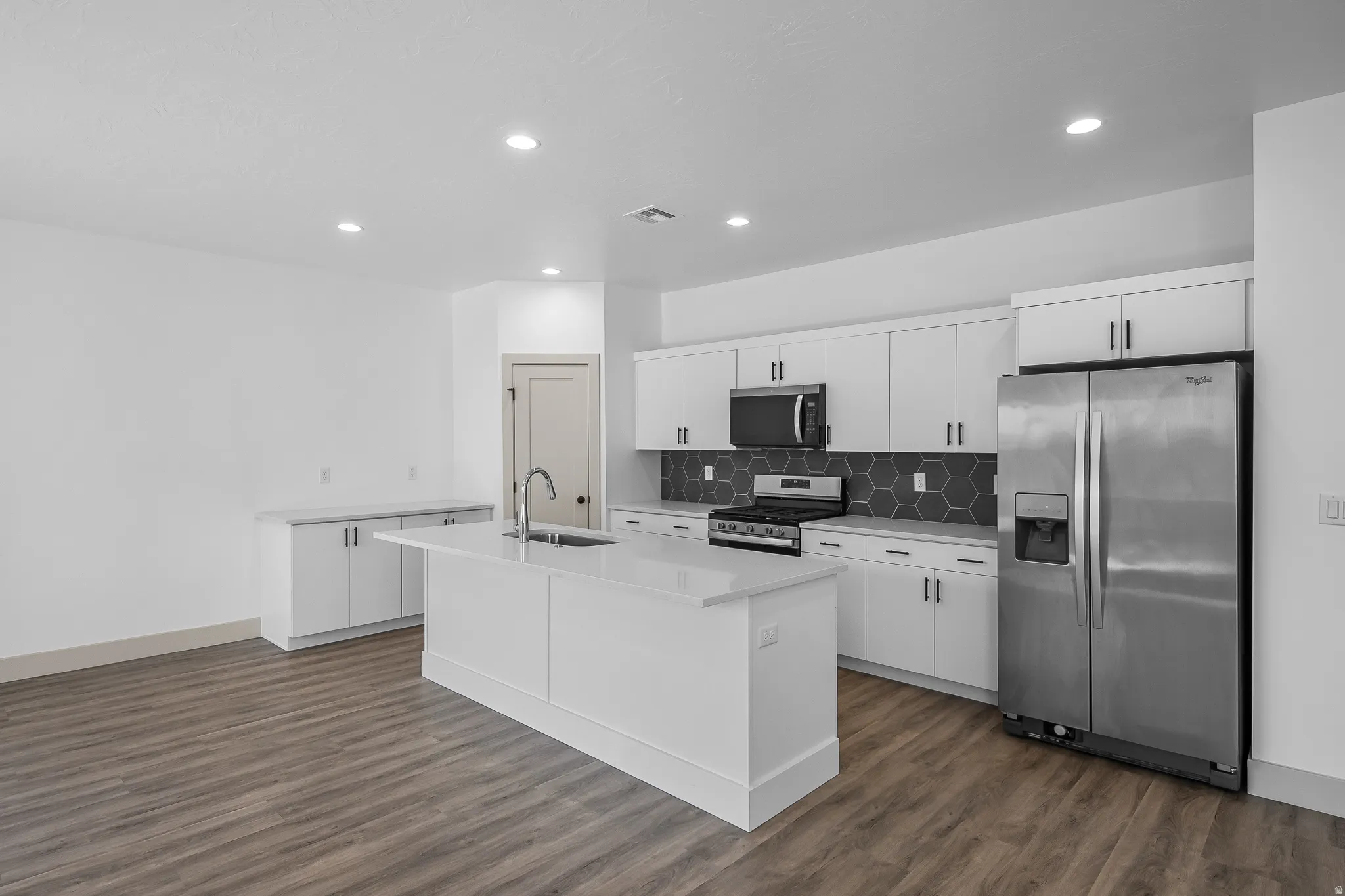 Kitchen featuring stainless steel appliances, white cabinetry, a kitchen island with sink, dark wood finished floors, and backsplash