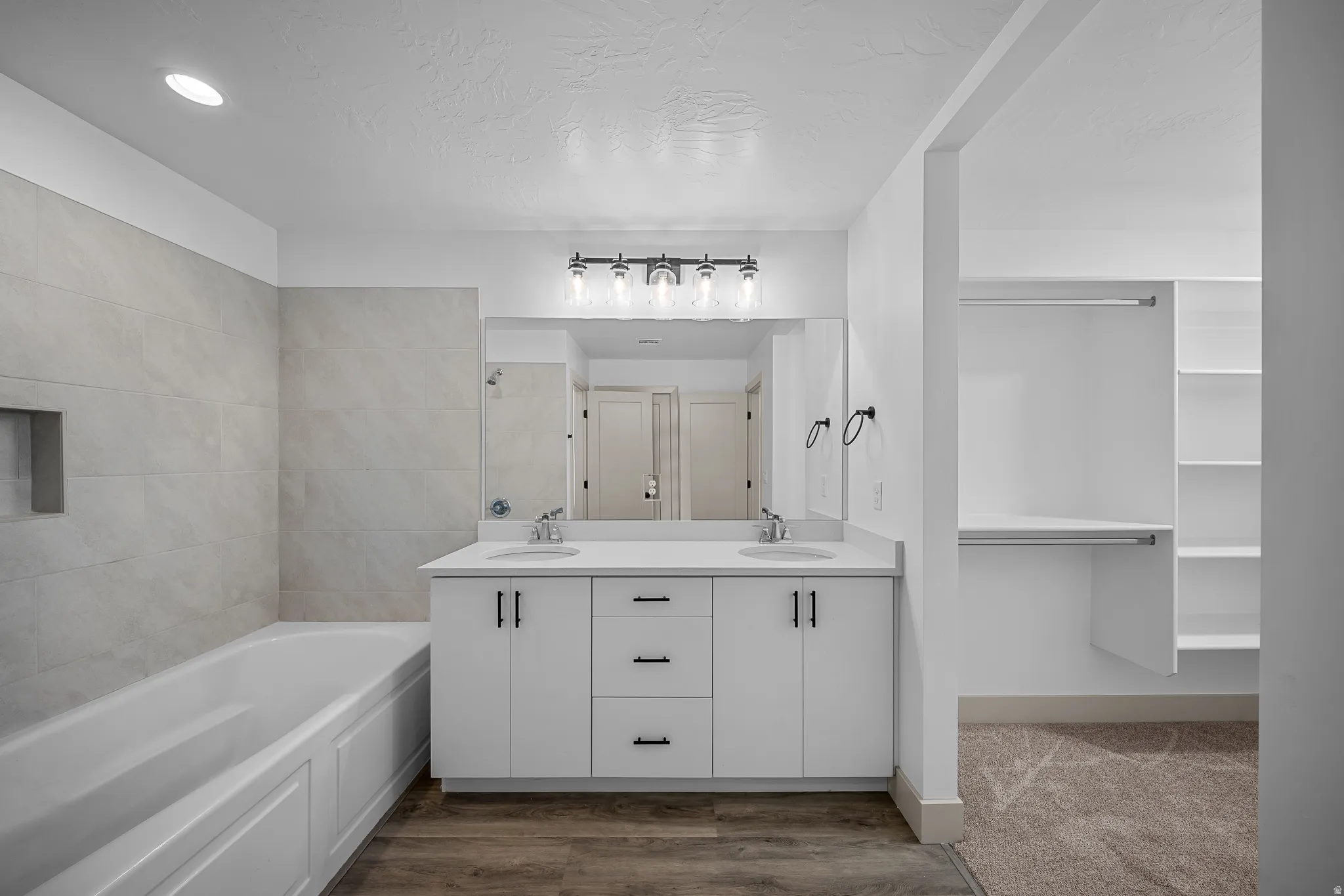 Bathroom with double vanity, a garden tub, dark wood-type flooring, and a textured ceiling