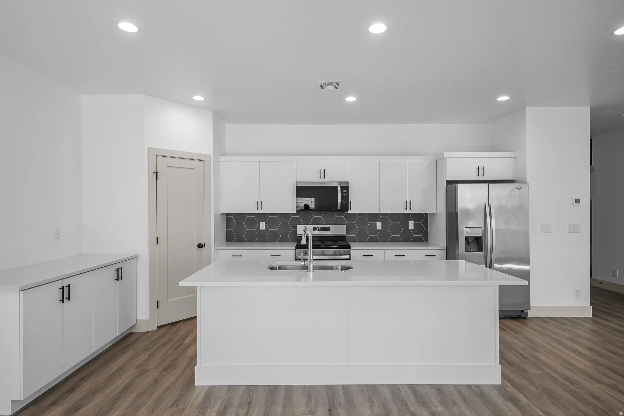 Kitchen with white cabinets, stainless steel appliances, dark wood-style floors, a kitchen island with sink, and light stone counters