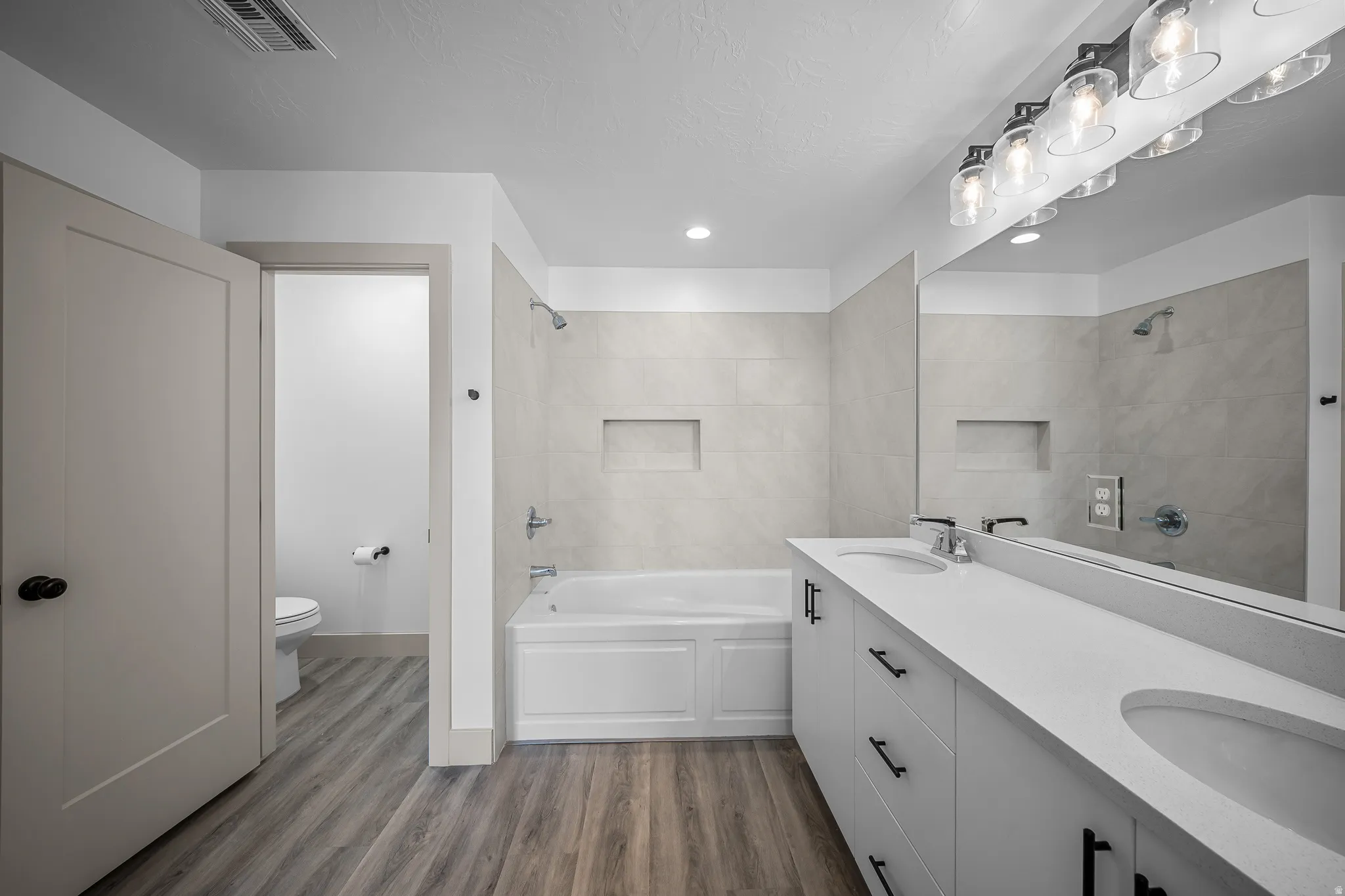 Bathroom with double vanity, dark wood-style floors,  shower combination, and recessed lighting