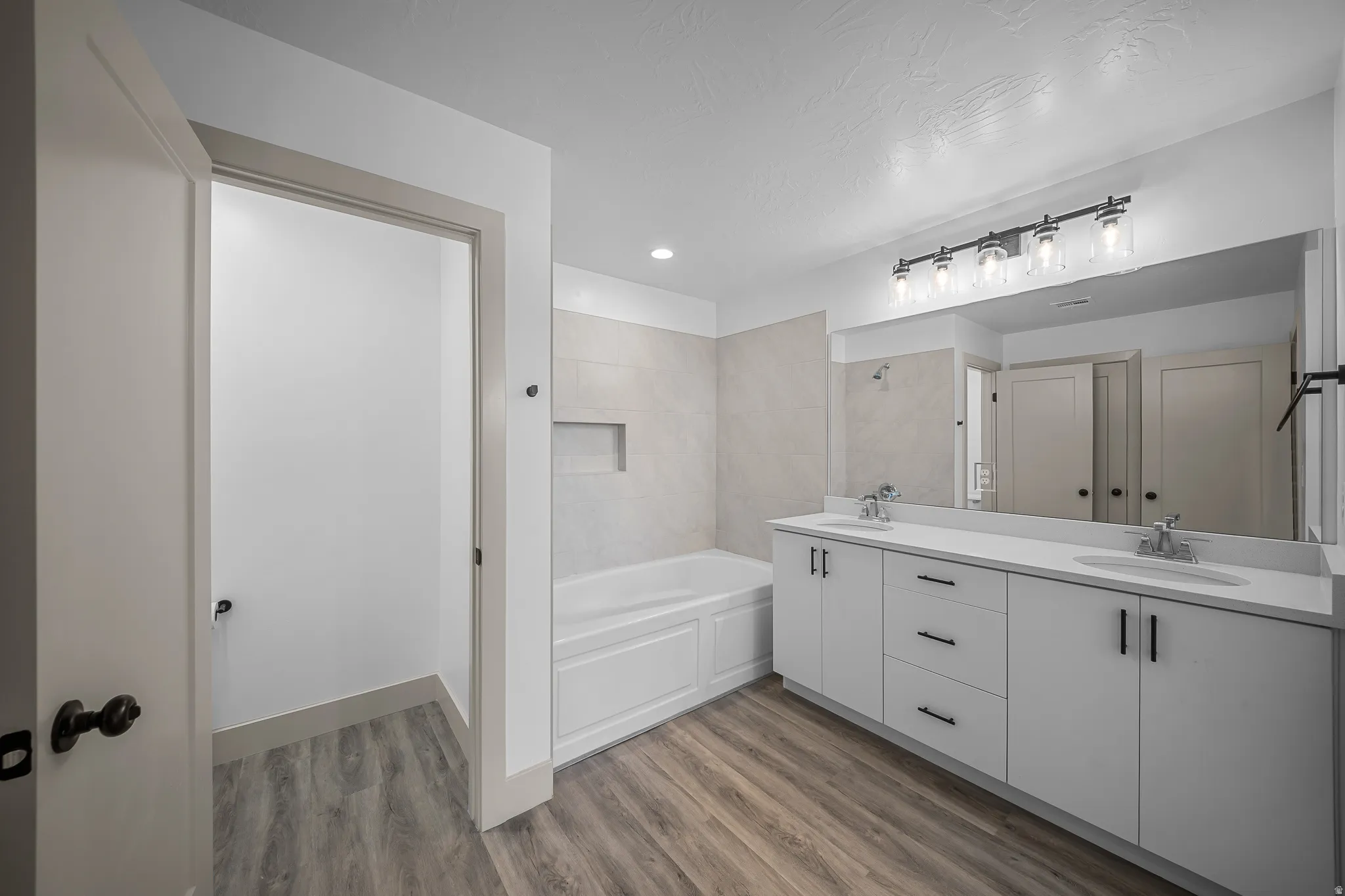 Bathroom featuring double vanity, a garden tub, dark wood-style floors, and recessed lighting