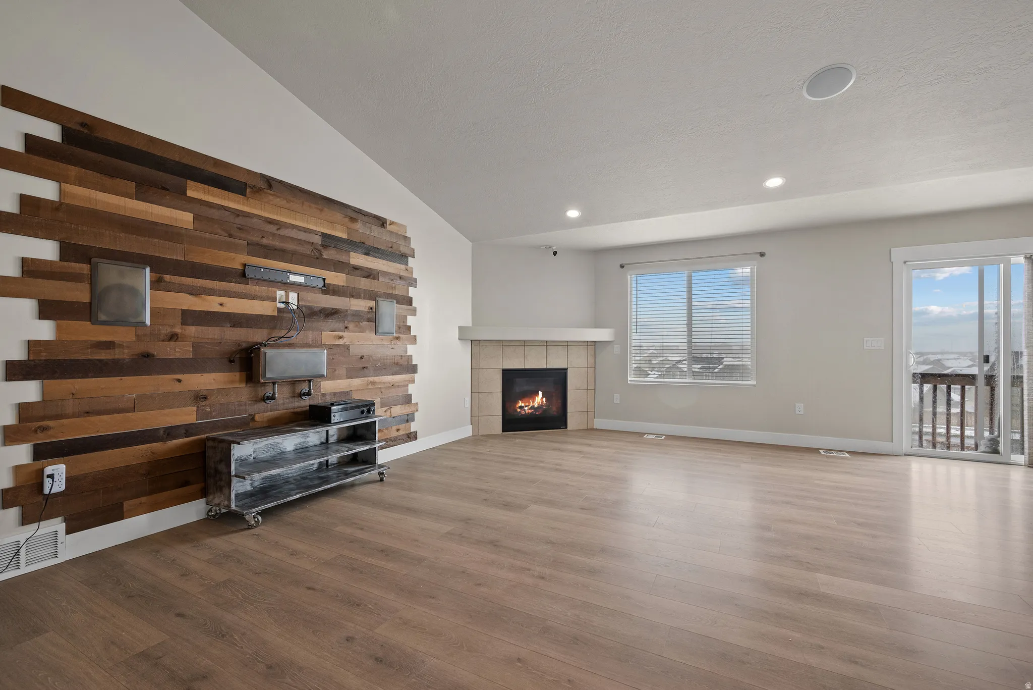 Unfurnished living room featuring a tile fireplace, wood finished floors, and lofted ceiling