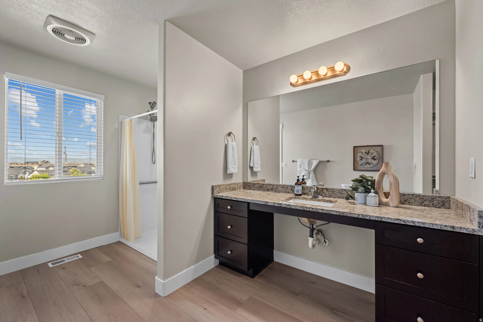 Spacious bathroom featuring an extended dark wood vanity with a light-toned stone countertop, an integrated rectangular sink, and a large wall-mounted mirror