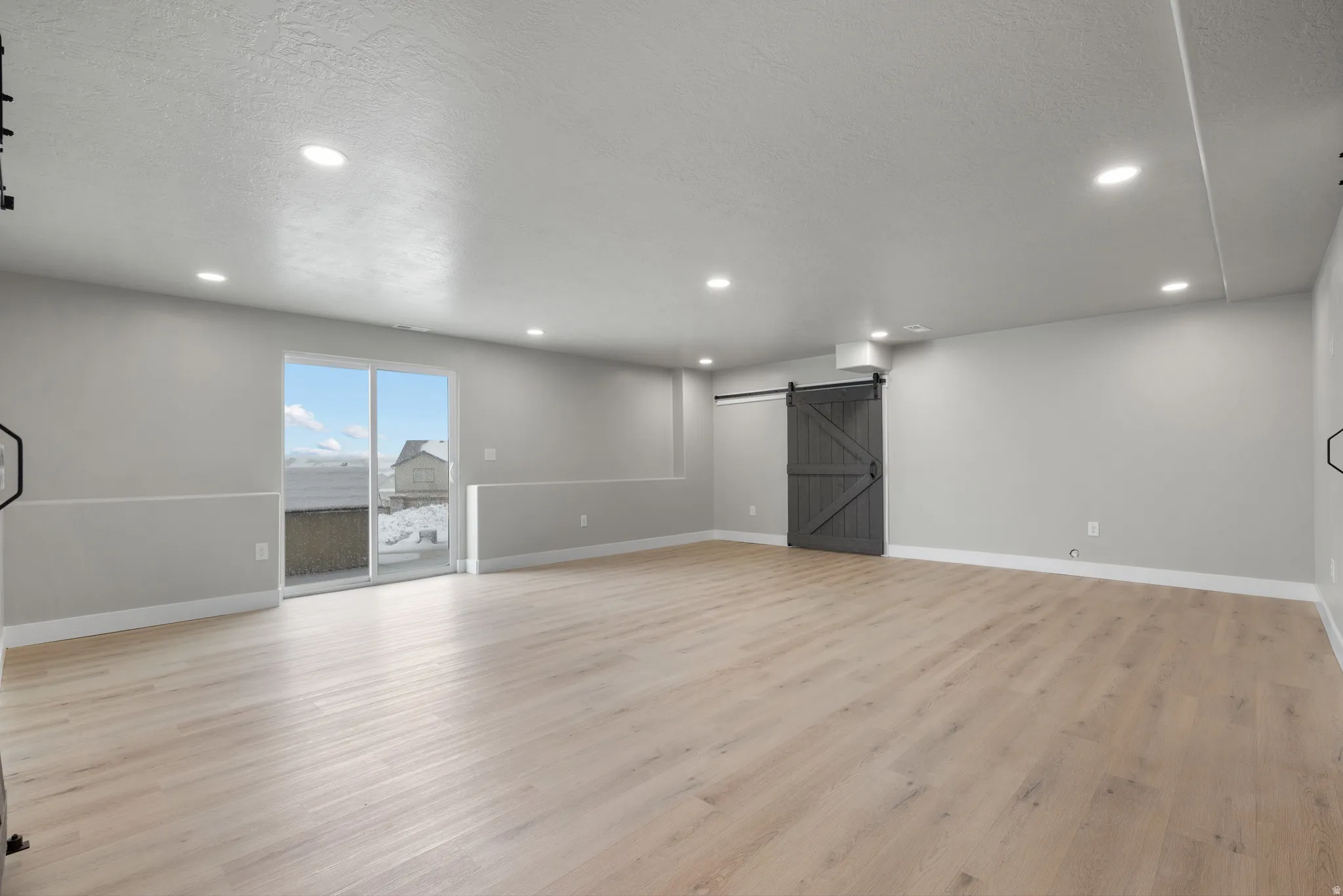 Basement with a barn door, light wood-type flooring, a textured ceiling, and recessed lighting