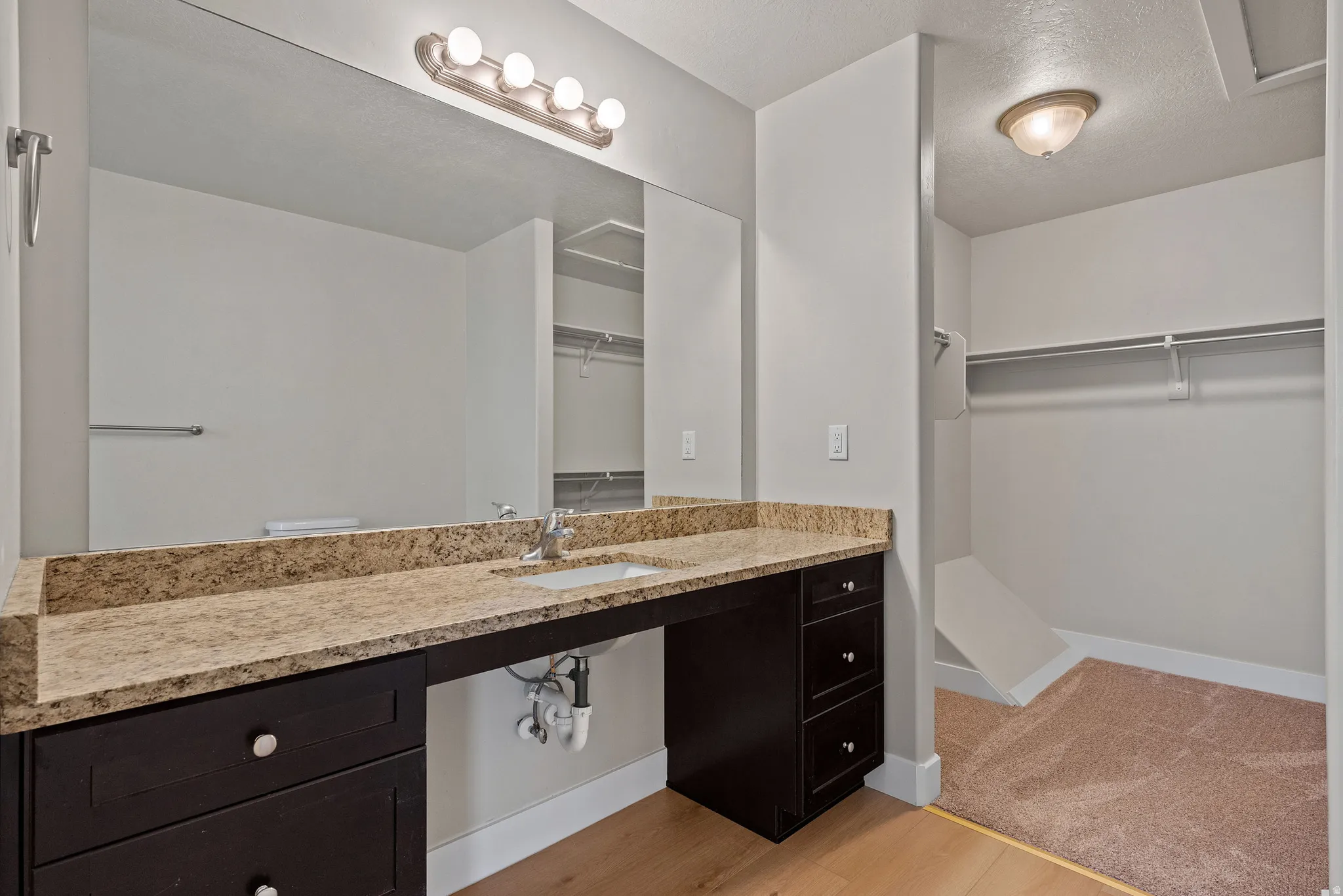 Bathroom with a walk in closet, vanity, a textured ceiling, and light wood-style floors