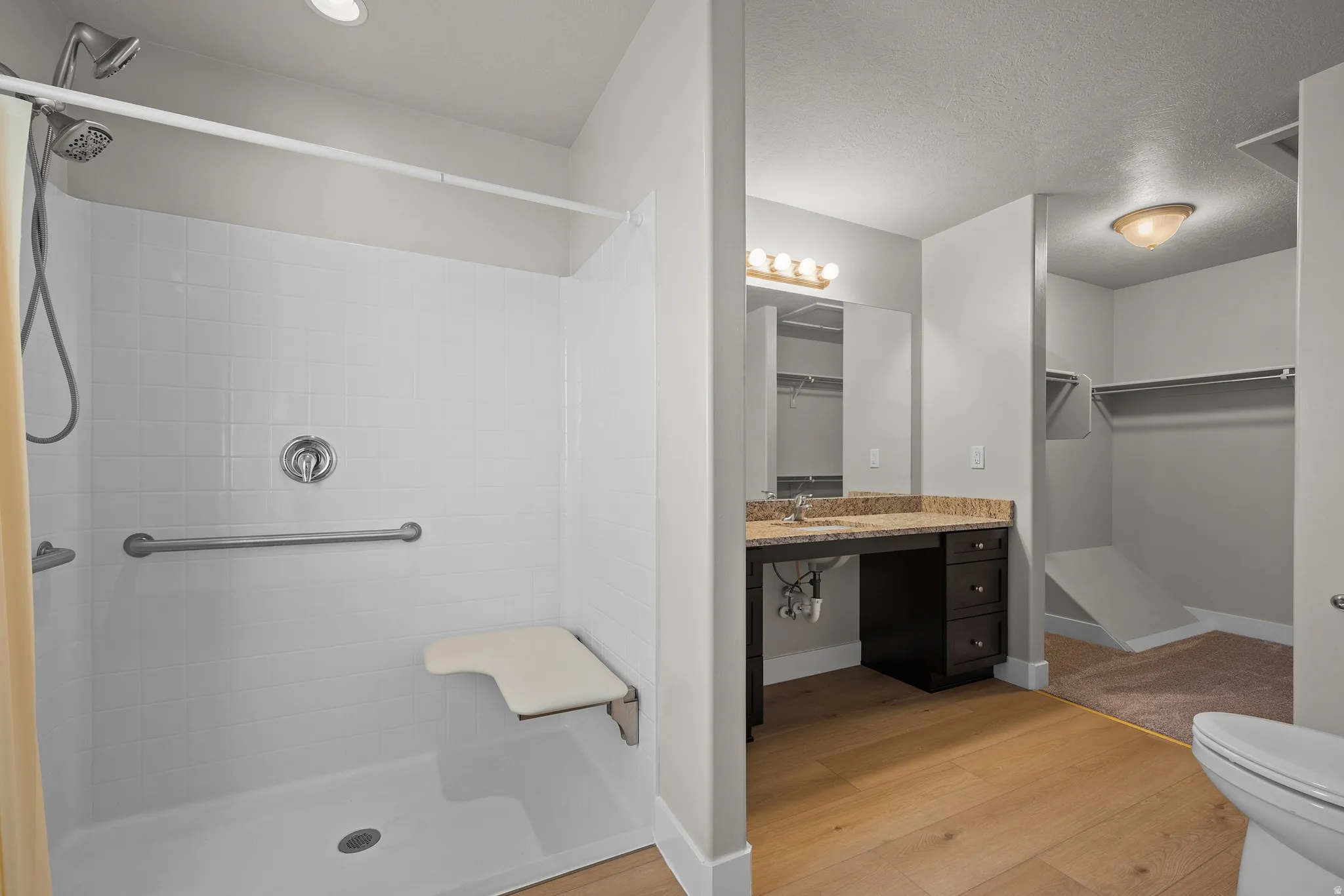 Bathroom featuring light wood-style flooring, a shower stall, vanity, and a spacious closet