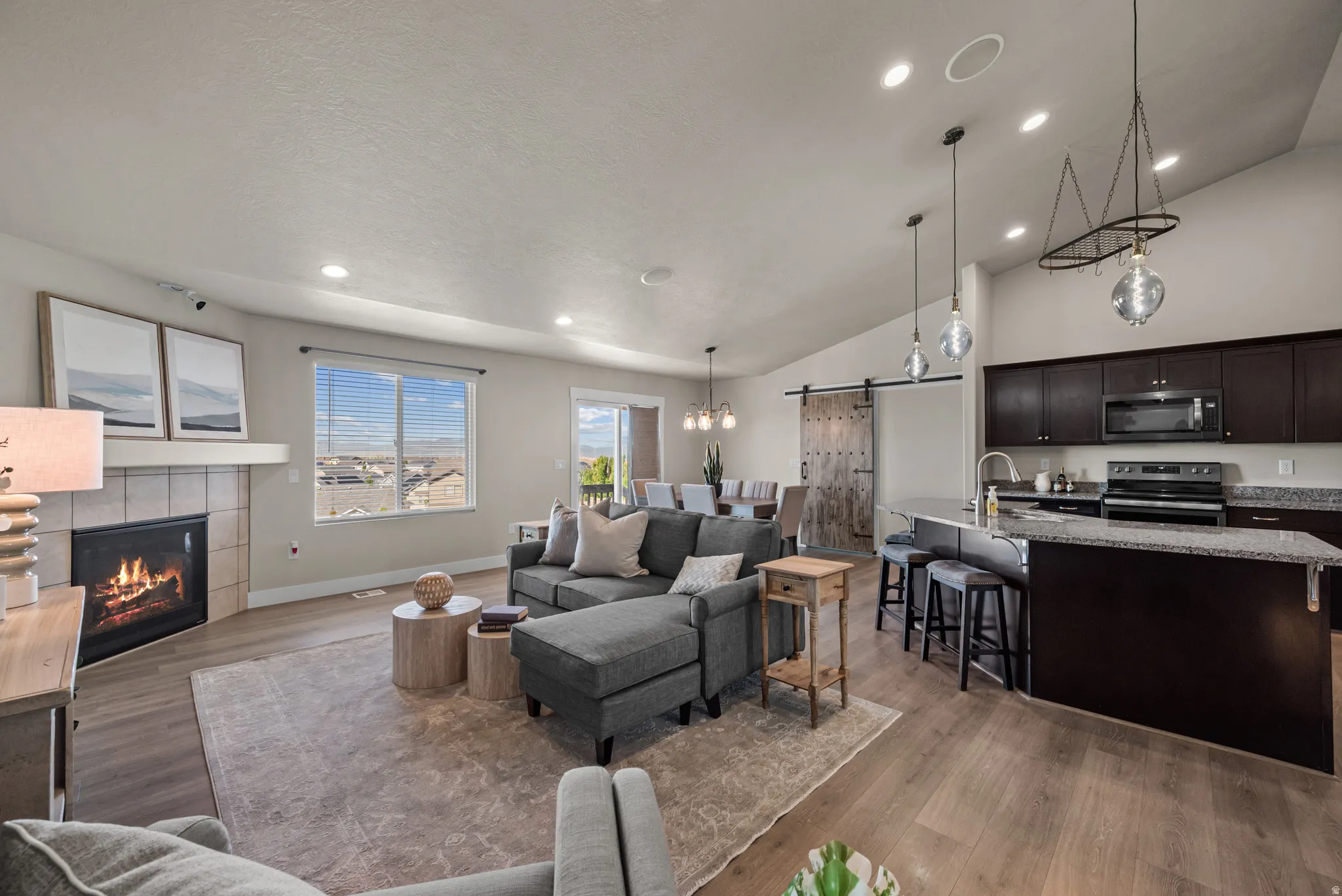 Open-concept living space featuring wood-finish flooring, a tiled fireplace with a mantel, and recessed ceiling lighting