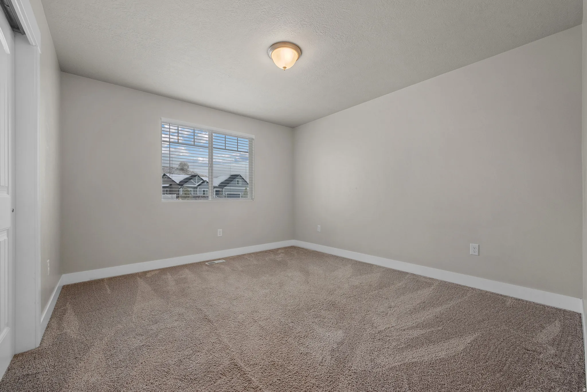 Empty room with light colored carpet and a textured ceiling