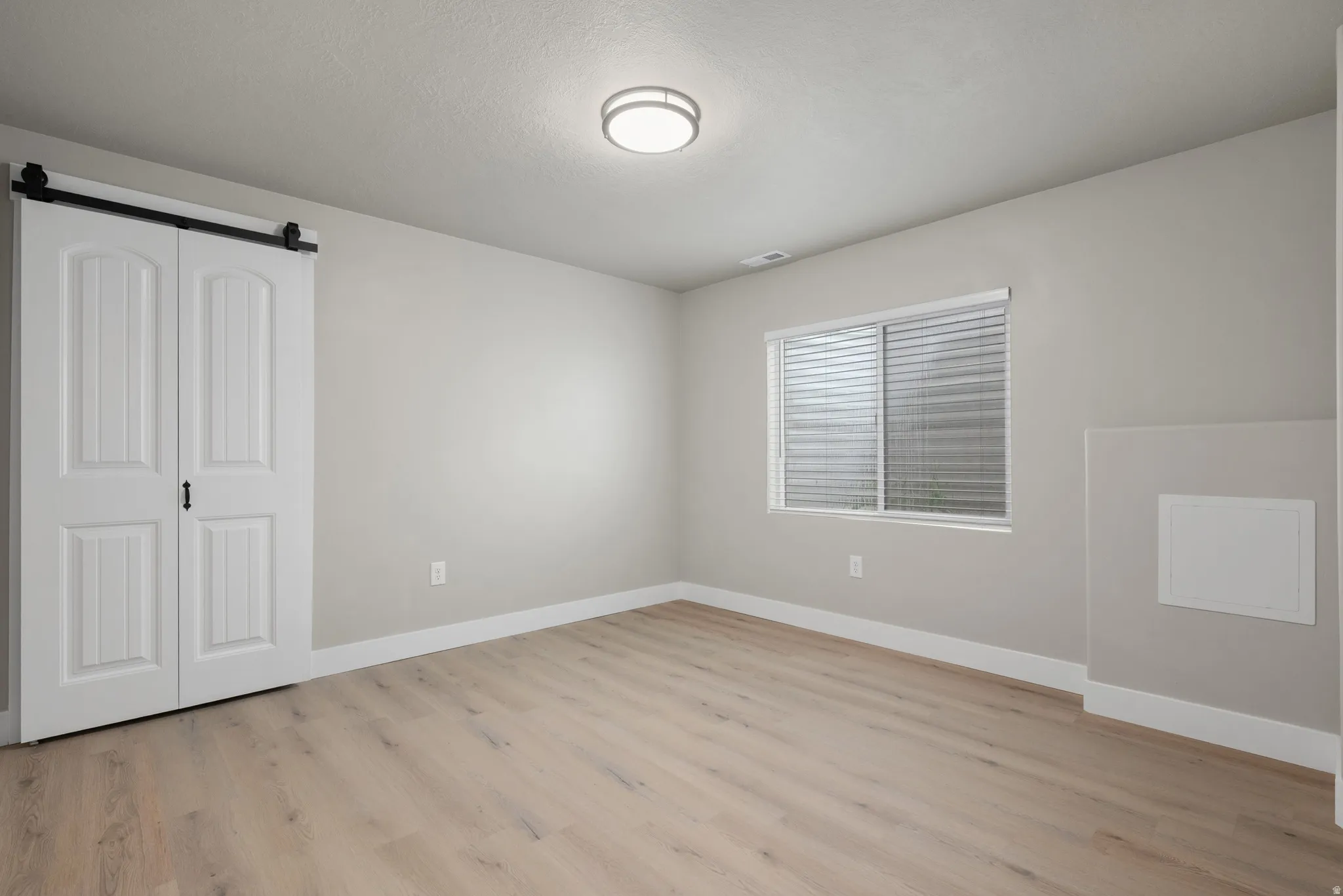 Unfurnished bedroom featuring light wood-style flooring, a barn door, and a closet