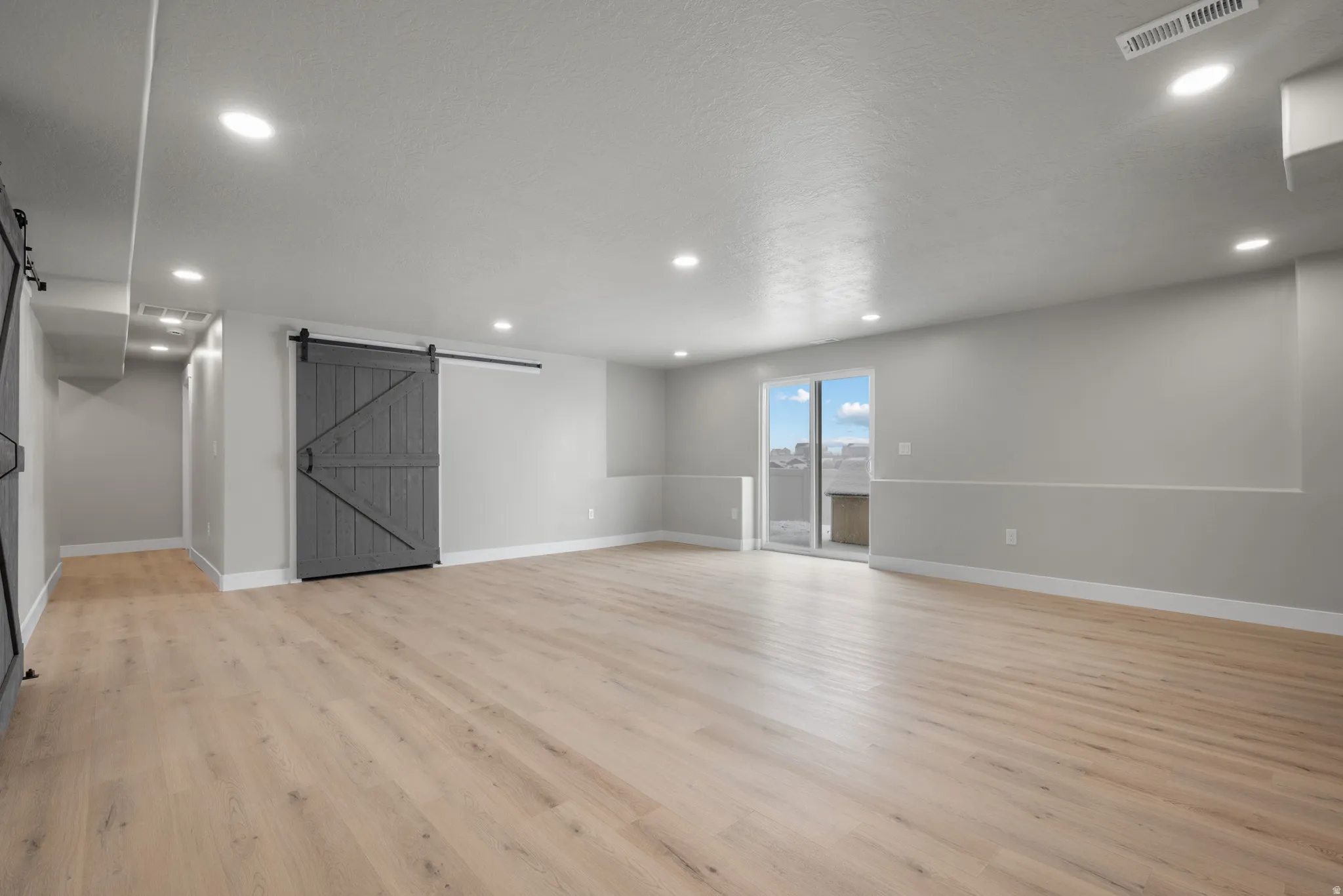 Unfurnished room with a barn door, recessed lighting, light wood-type flooring, and a textured ceiling