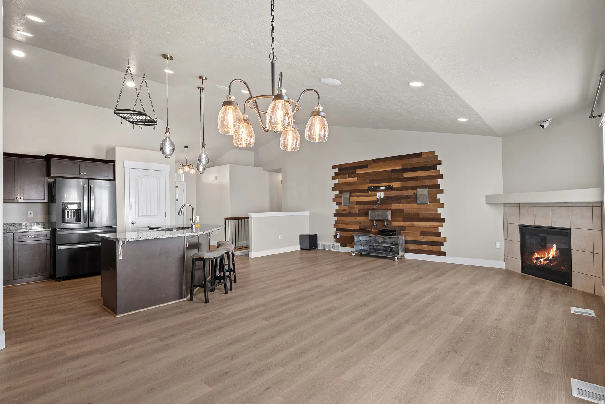 Kitchen with open floor plan, dark wood finish cabinetry, stainless steel refrigerator with ice dispenser, a kitchen bar, and light stone counters