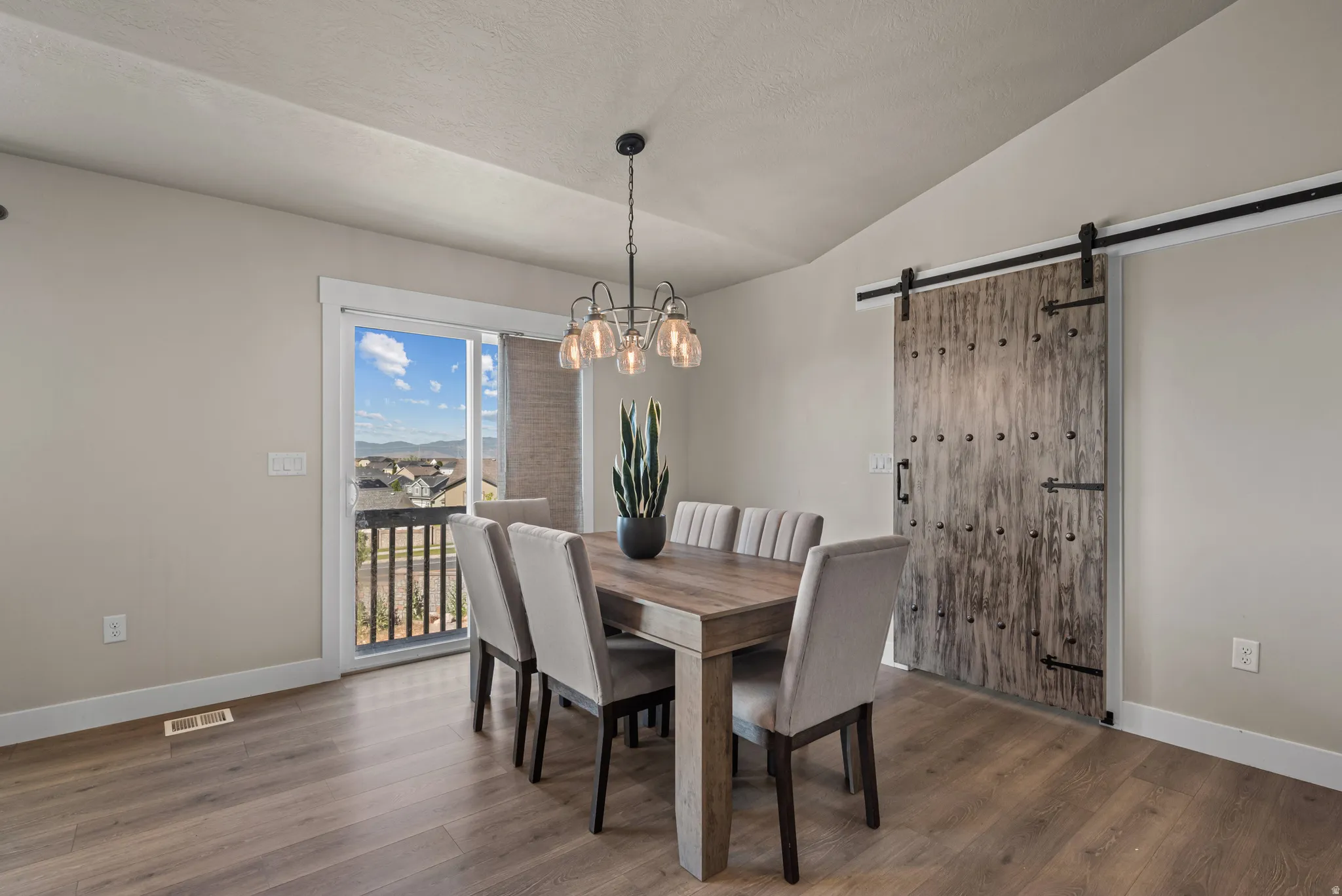Dining area featuring wood-finish flooring, a contemporary chandelier, and a sliding barn door with dark hardware