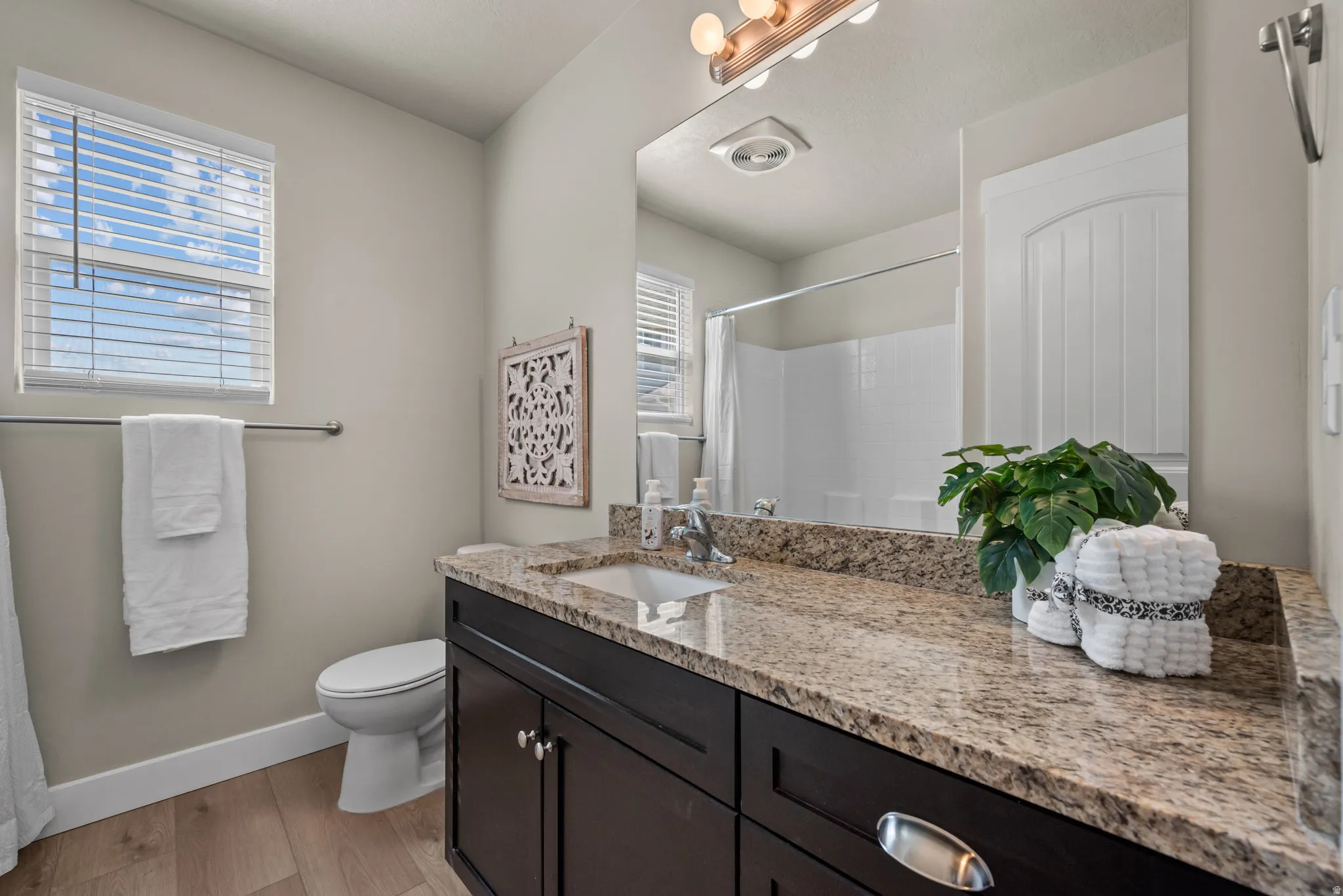 Bathroom vanity featuring a light-toned granite countertop, undermount sink, and dark wood-finish cabinetry with silver-tone hardware