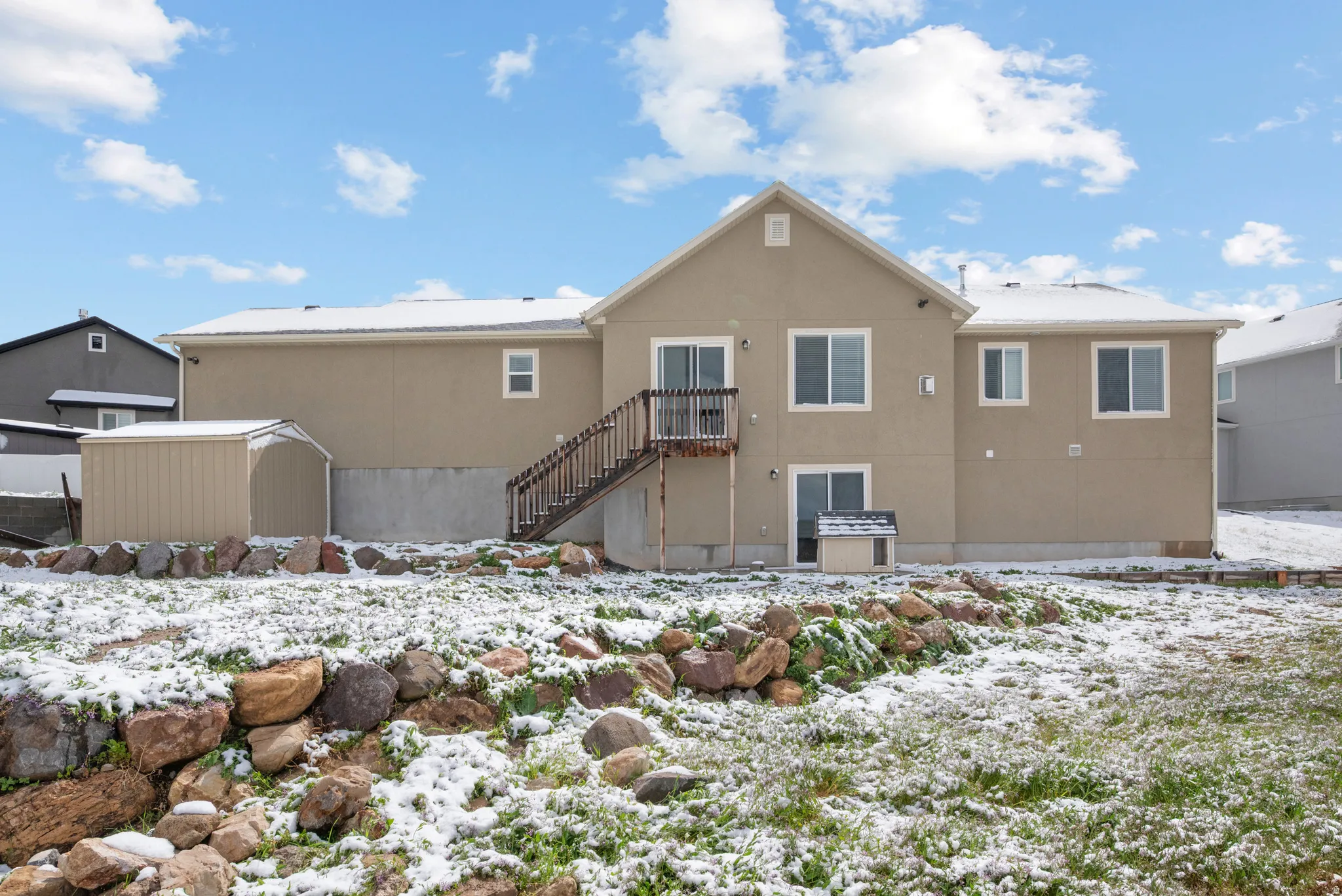 Snow covered rear of property with stucco siding and a storage shed
