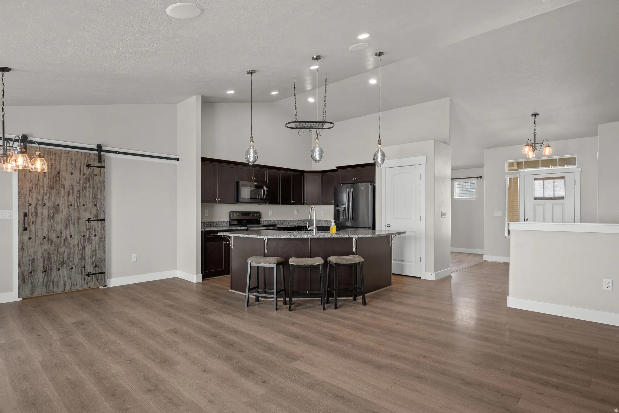 Kitchen featuring a chandelier, a barn door, an island with sink, black appliances, and a kitchen bar