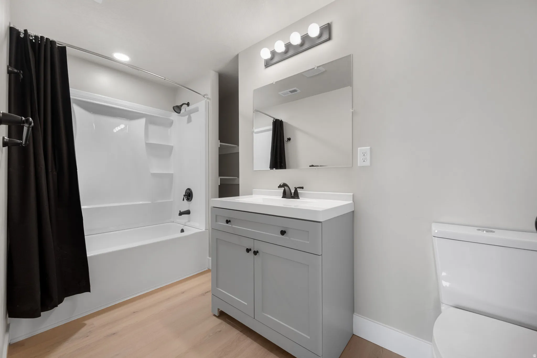 Full bath with shower / bathtub combination with curtain, vanity, and light wood-type flooring
