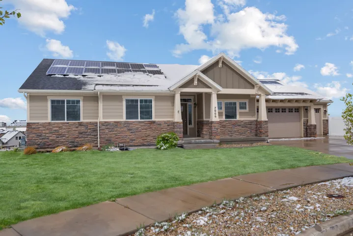 View of front of house featuring solar panels, an attached garage, a front yard, stone siding, and concrete driveway