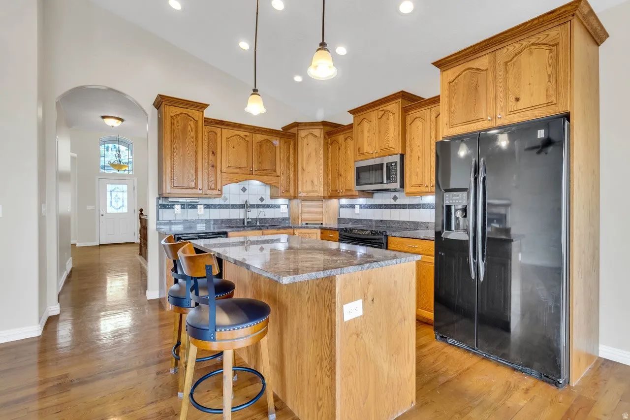 Kitchen with arched walkways, black appliances, backsplash, dark stone countertops, and lofted ceiling