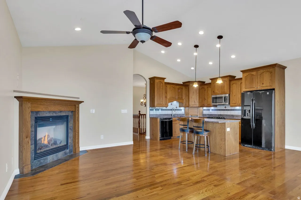 Kitchen featuring wood finish cabinets, arched walkways, black appliances, a center island, and light wood-style floors