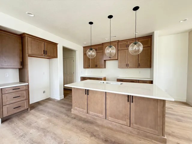 Kitchen with wood finish cabinetry, light wood-type flooring, light stone countertops, a center island, and pendant lighting