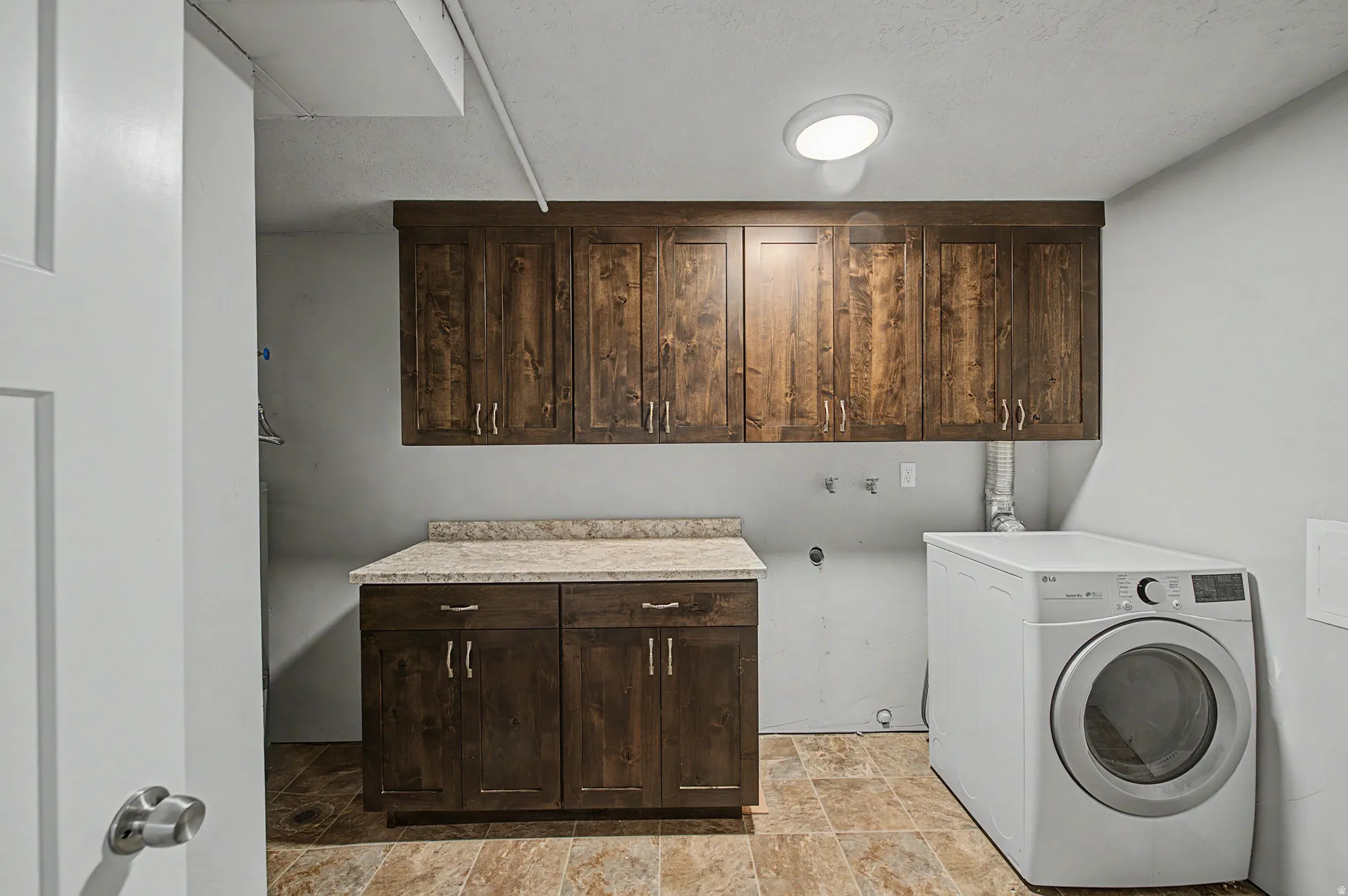 Laundry area featuring washer / clothes dryer, cabinet space, stone finish floors, and a textured ceiling