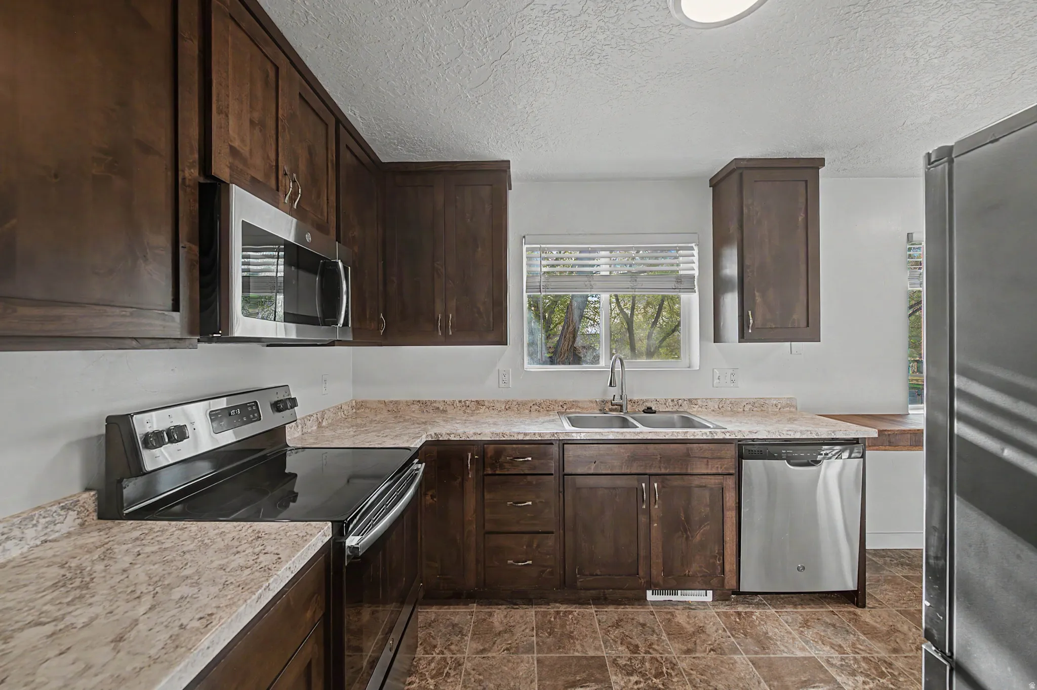 Kitchen featuring dark wood finish cabinets, stainless steel appliances, light countertops, and a textured ceiling