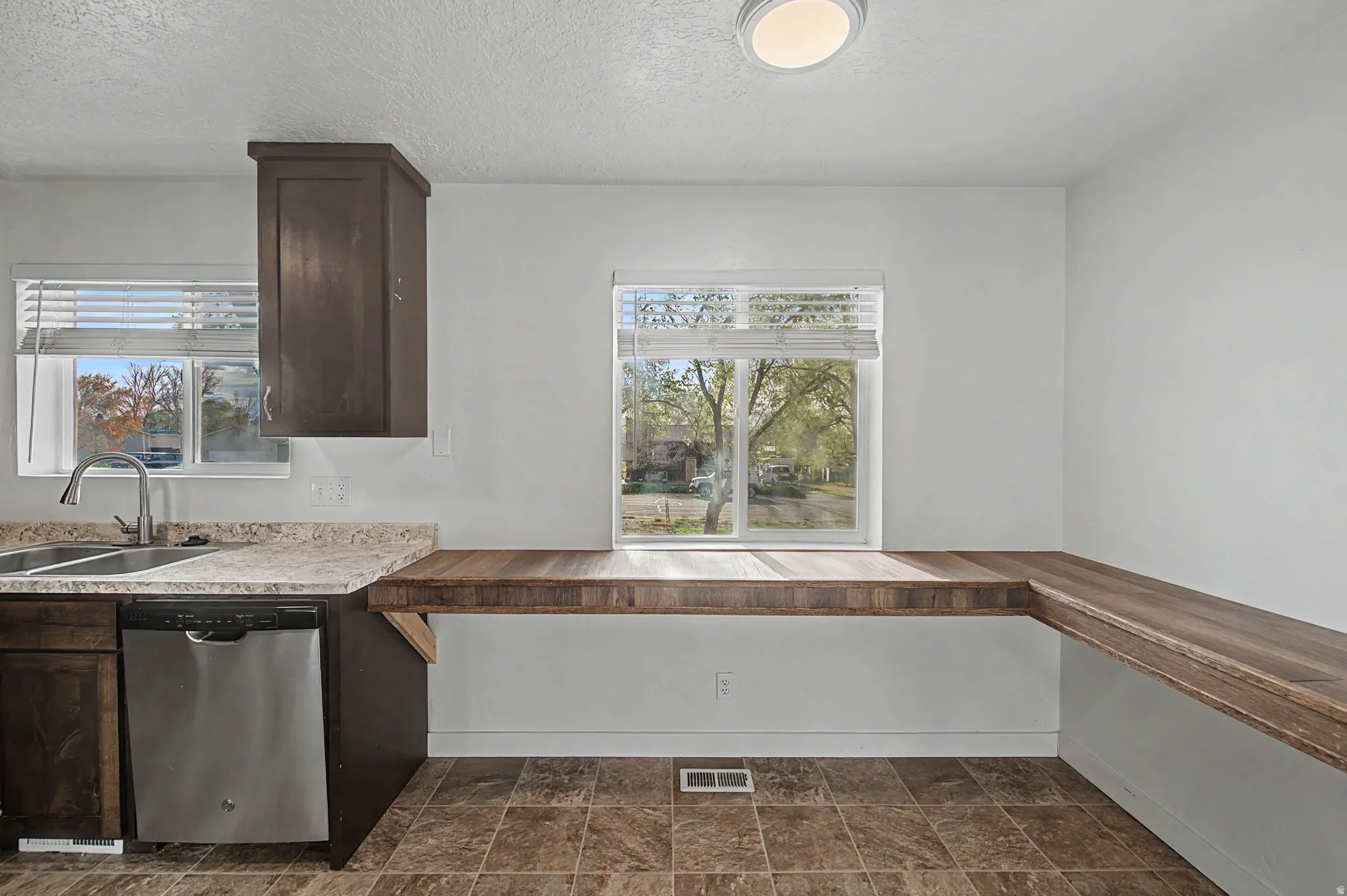 Kitchen with dark wood finish cabinets, dishwasher, stone finish floors, a textured ceiling, and light countertops