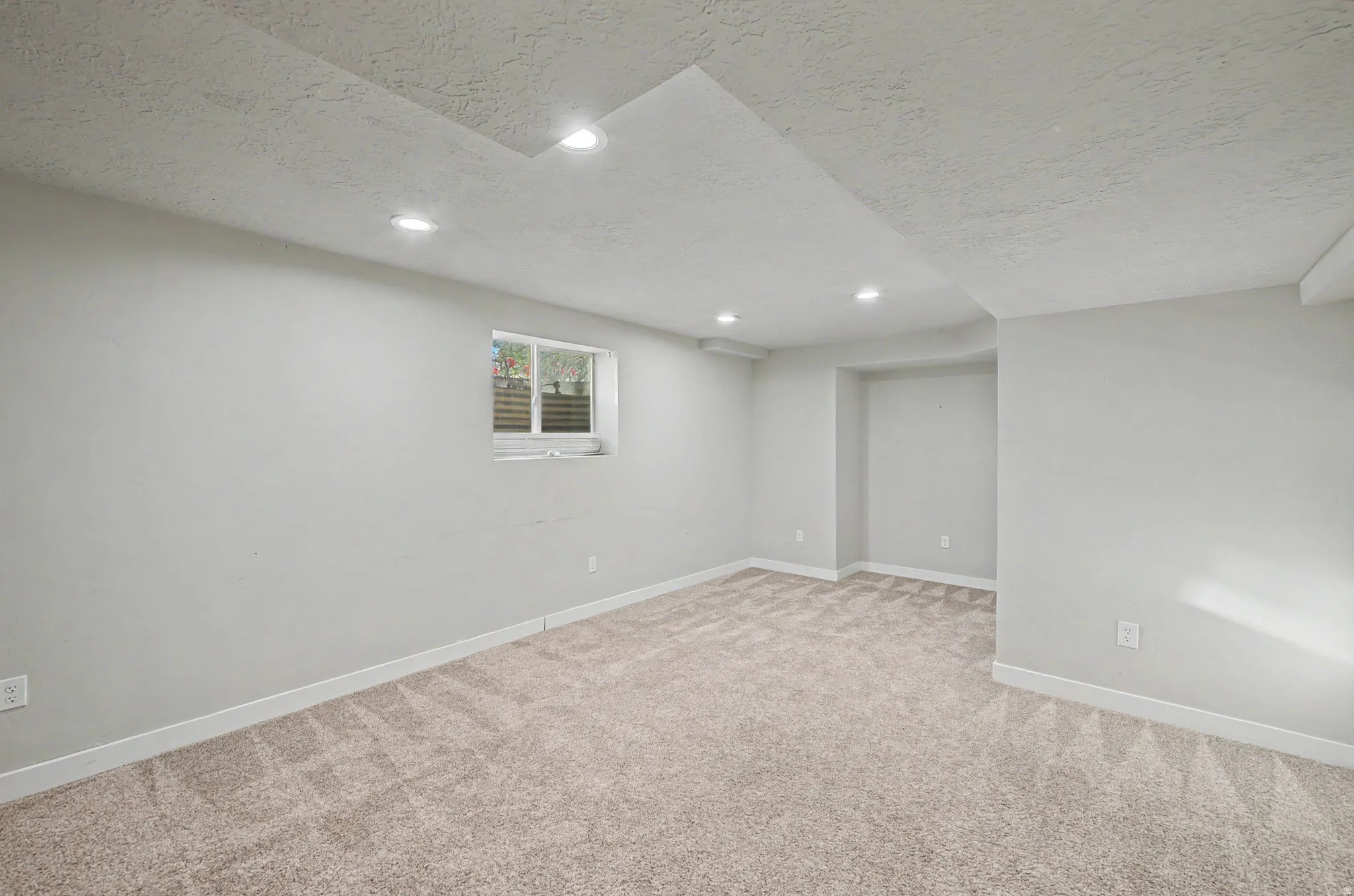 Below grade area featuring a textured ceiling, light carpet, and recessed lighting