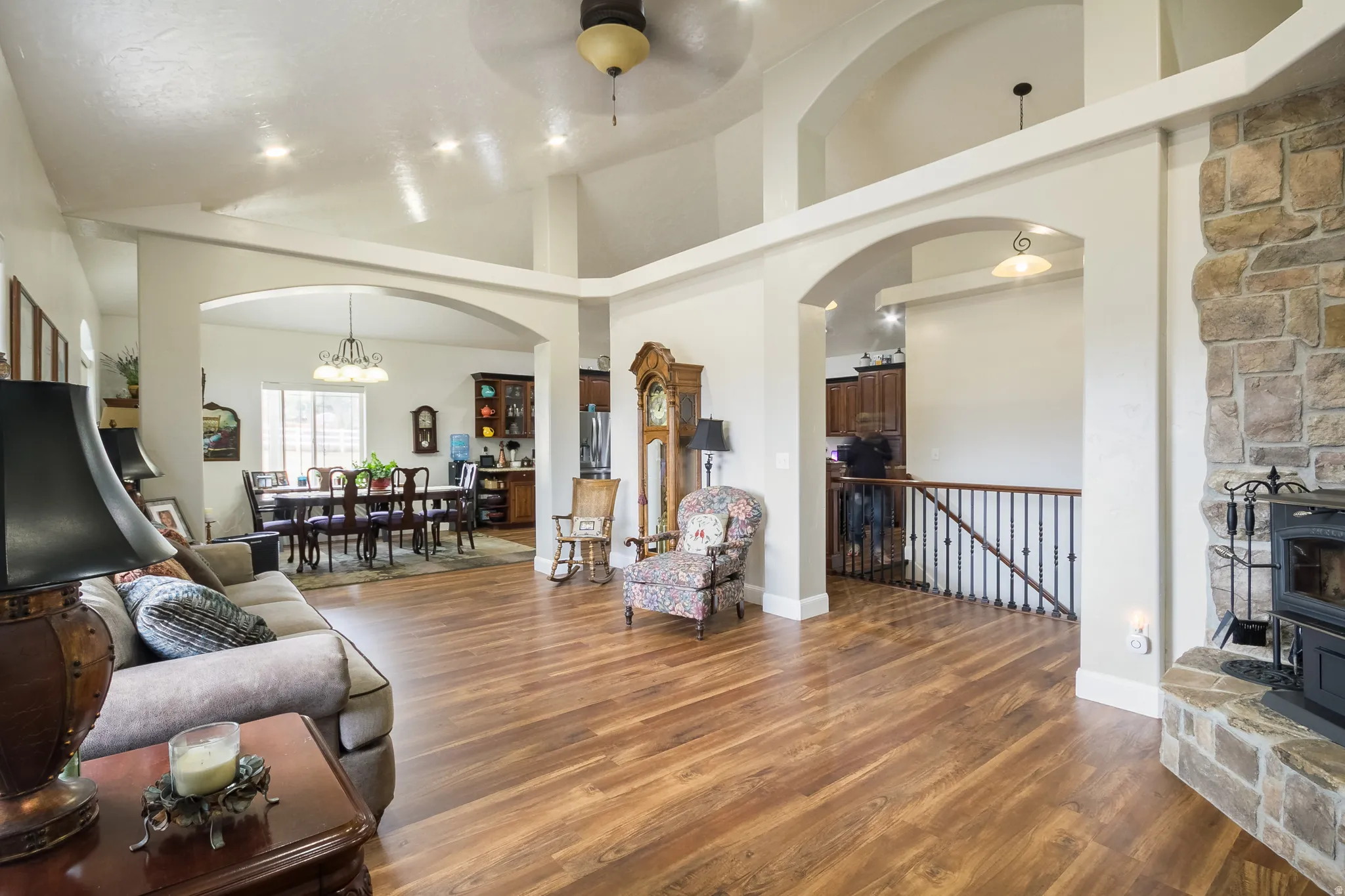 Living room featuring dark wood-style flooring, arched walkways, a ceiling fan, a high ceiling, and suspended lighting
