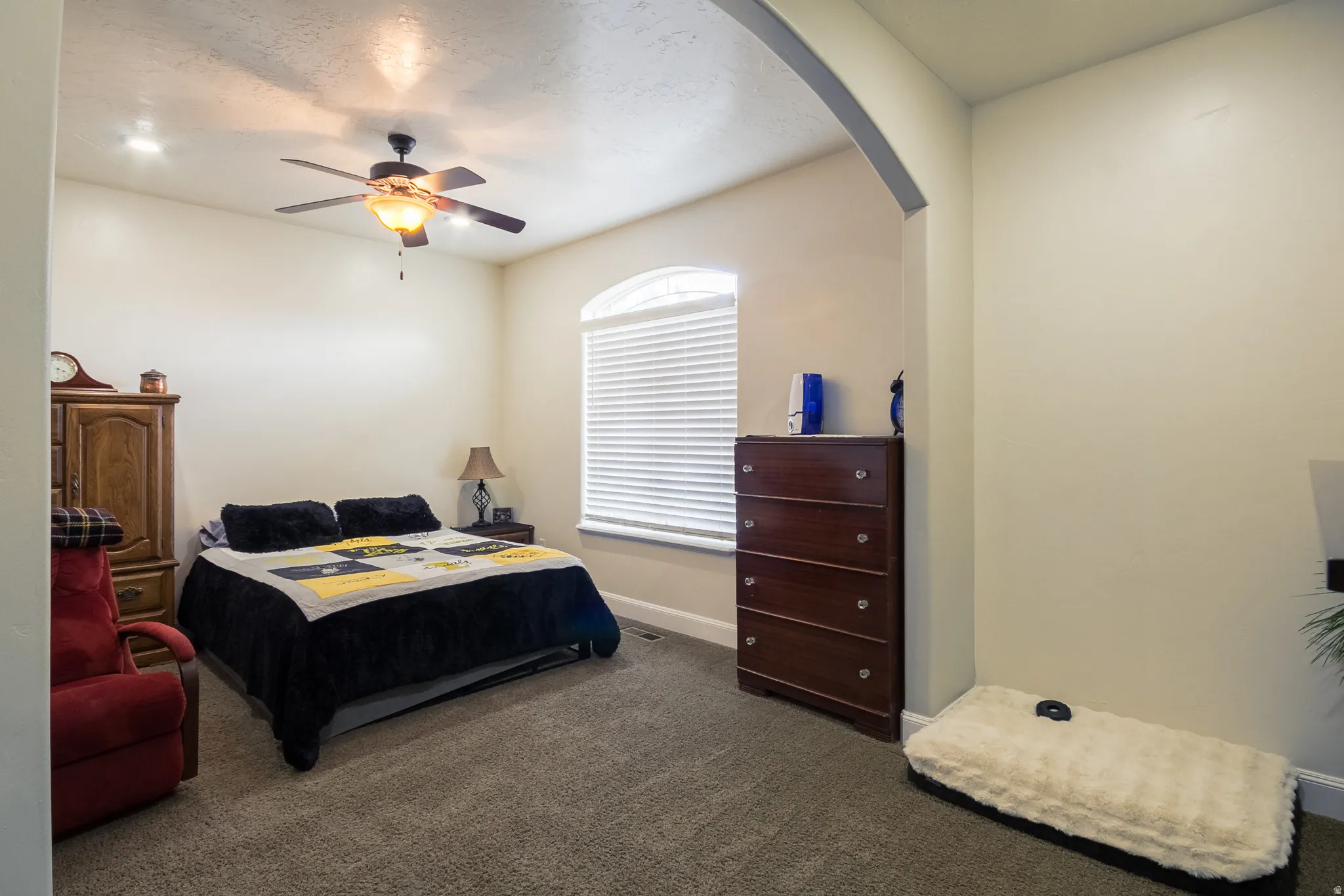 Bedroom with dark colored carpet, a ceiling fan, arched walkways, and a textured ceiling