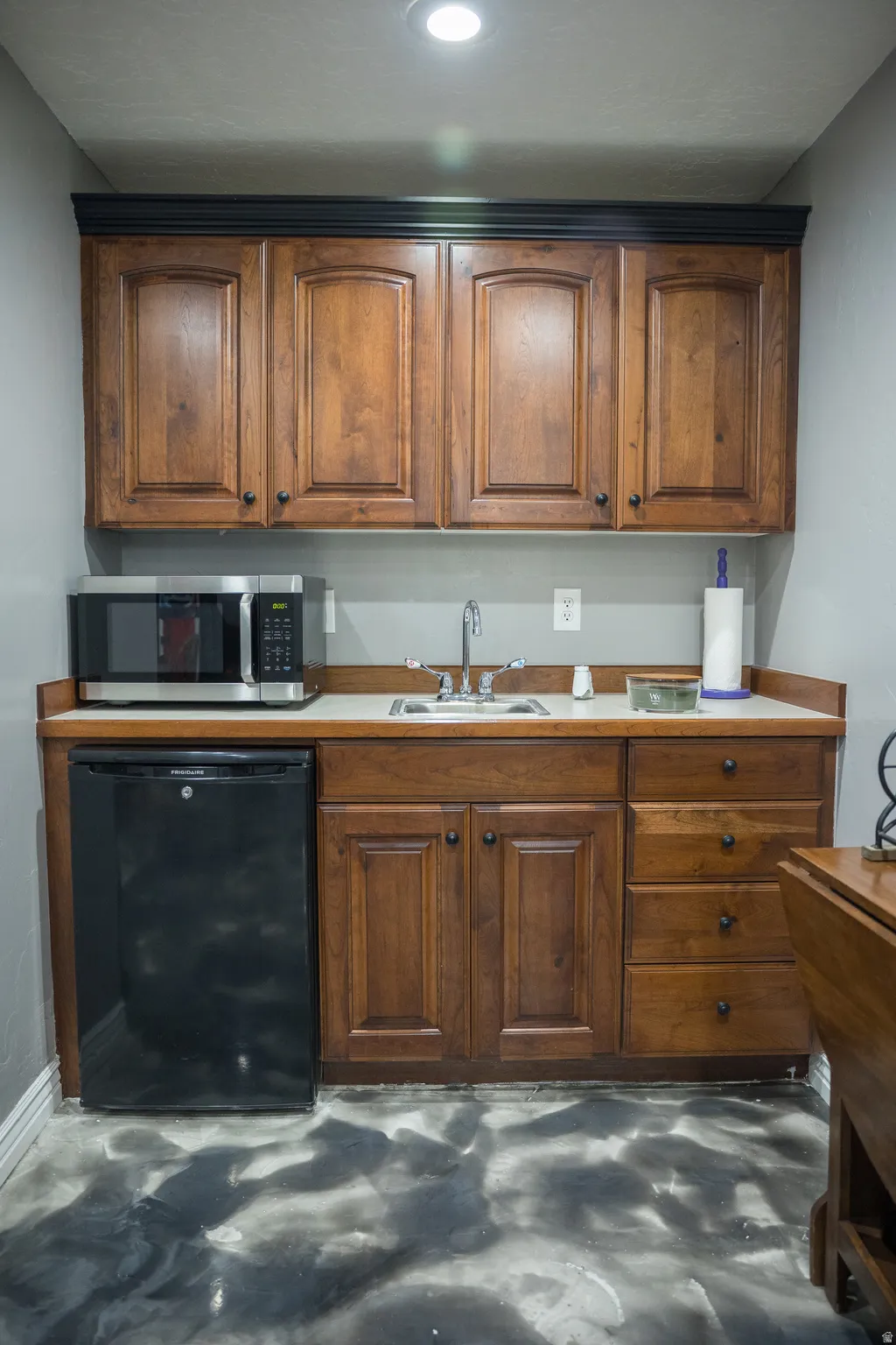 Kitchen with wood finish cabinetry, black dishwasher, stainless steel microwave, and concrete flooring