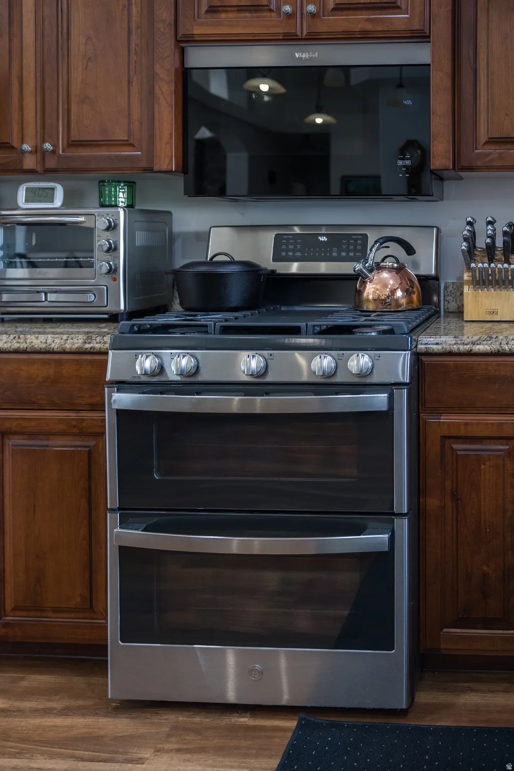 Kitchen with range with two ovens, dark wood finish cabinetry, black microwave, dark stone counters, and dark wood-type flooring