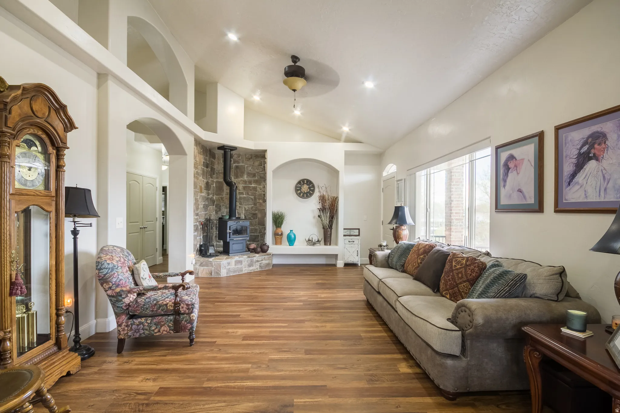 Living area featuring dark wood-style flooring, ceiling fan, lofted ceiling, a wood stove, and arched walkways