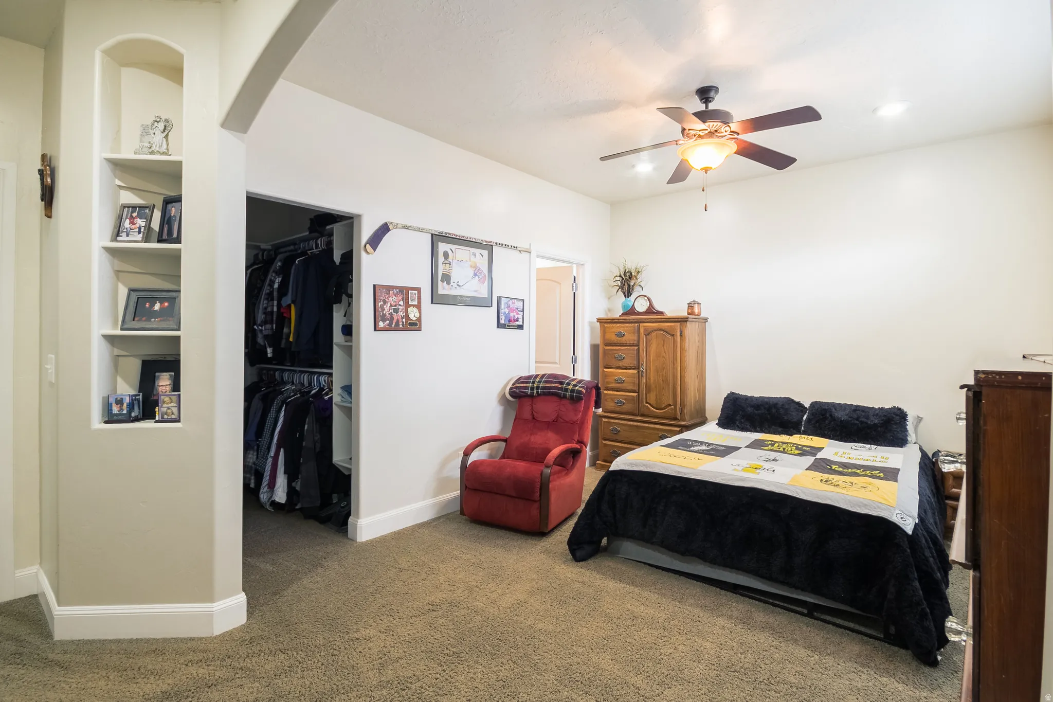 Carpeted bedroom with a walk in closet, arched walkways, and ceiling fan