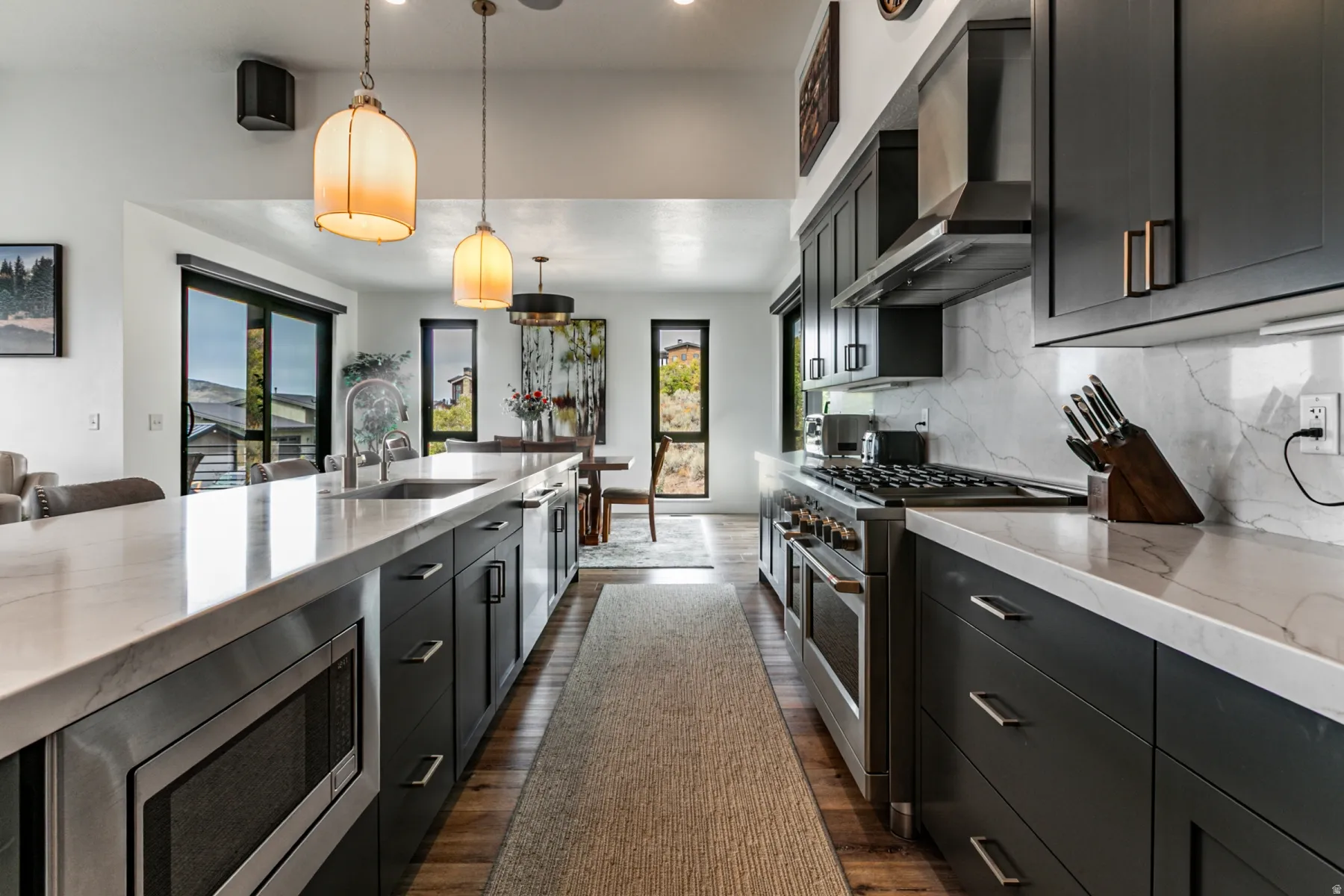 Kitchen featuring dark cabinets, stainless steel appliances, light stone countertops, decorative light fixtures, and dark wood finished floors