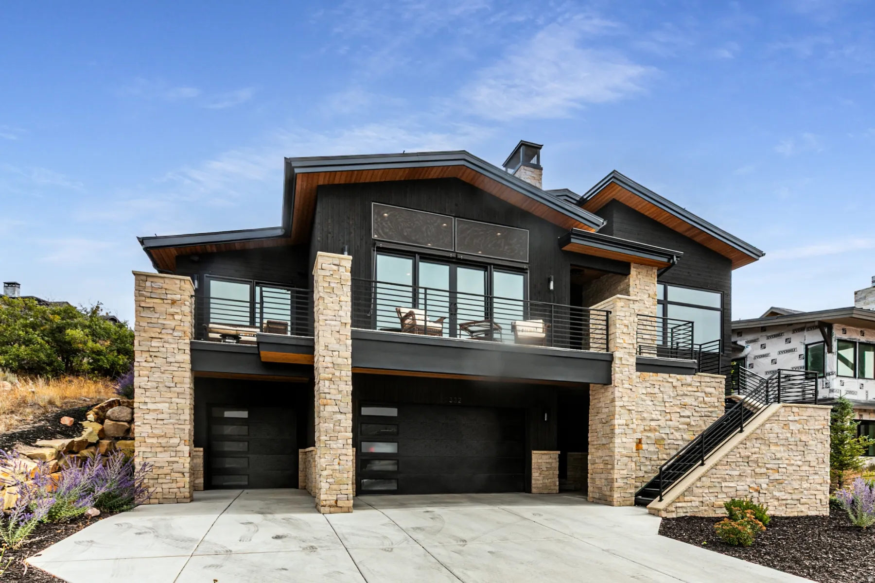 View of front of house featuring concrete driveway, a garage, stone siding, a balcony, and a chimney