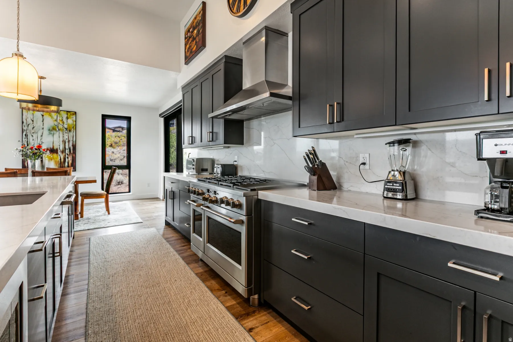 Kitchen featuring double oven range, light stone counters, dark wood-style flooring, backsplash, and hanging light fixtures
