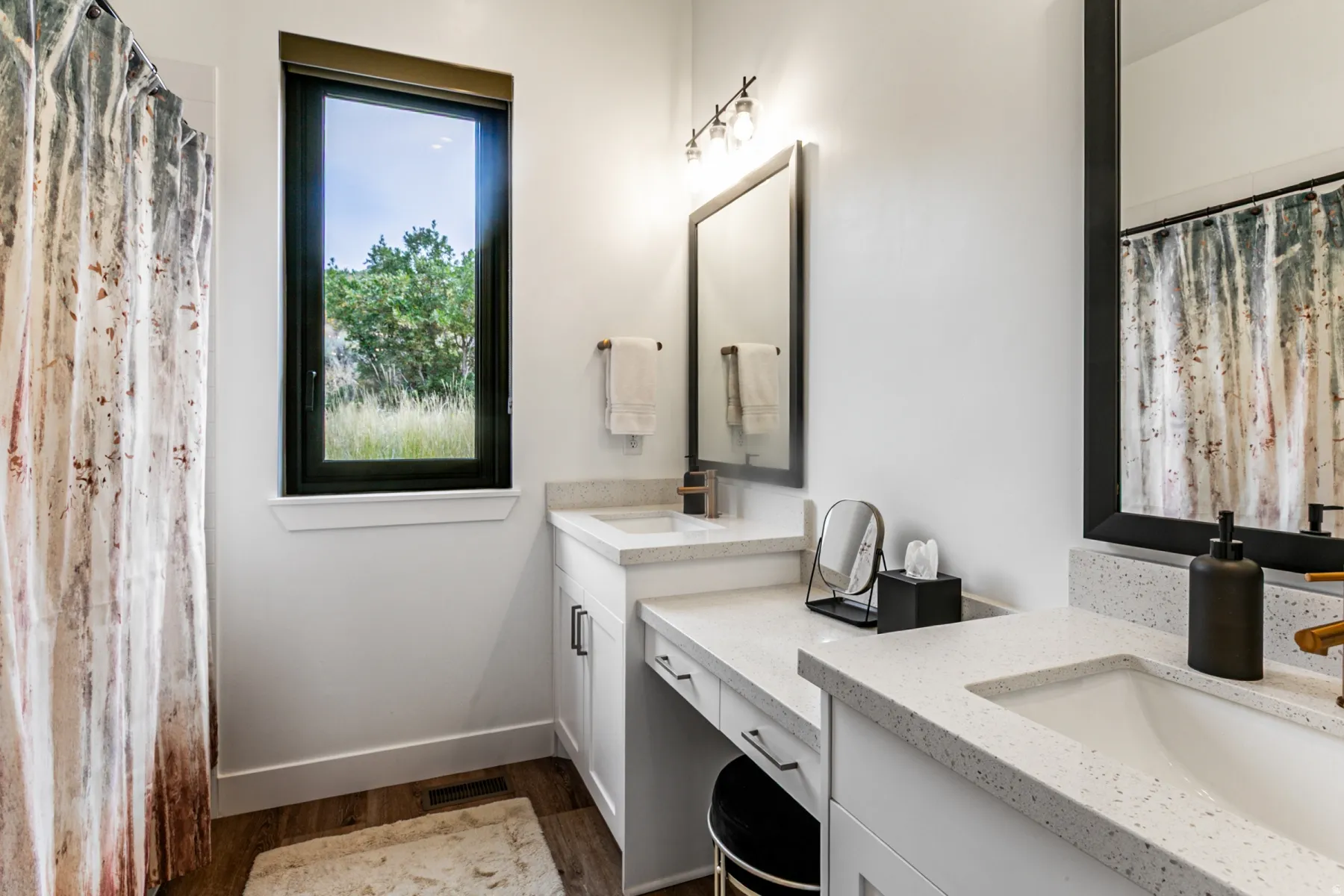 Bathroom featuring a shower with shower curtain, two vanities, and light wood-type flooring