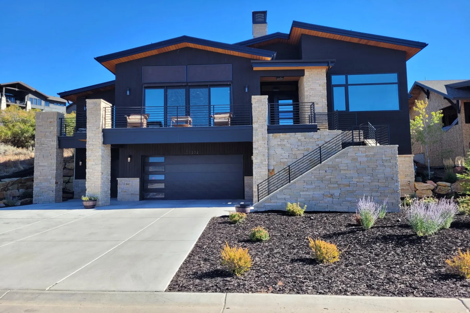 Modern home featuring a balcony, a garage, concrete driveway, and stone siding