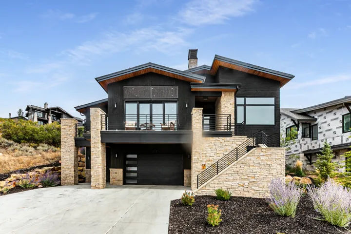 Contemporary home featuring stone siding, a balcony, driveway, a garage, and a chimney