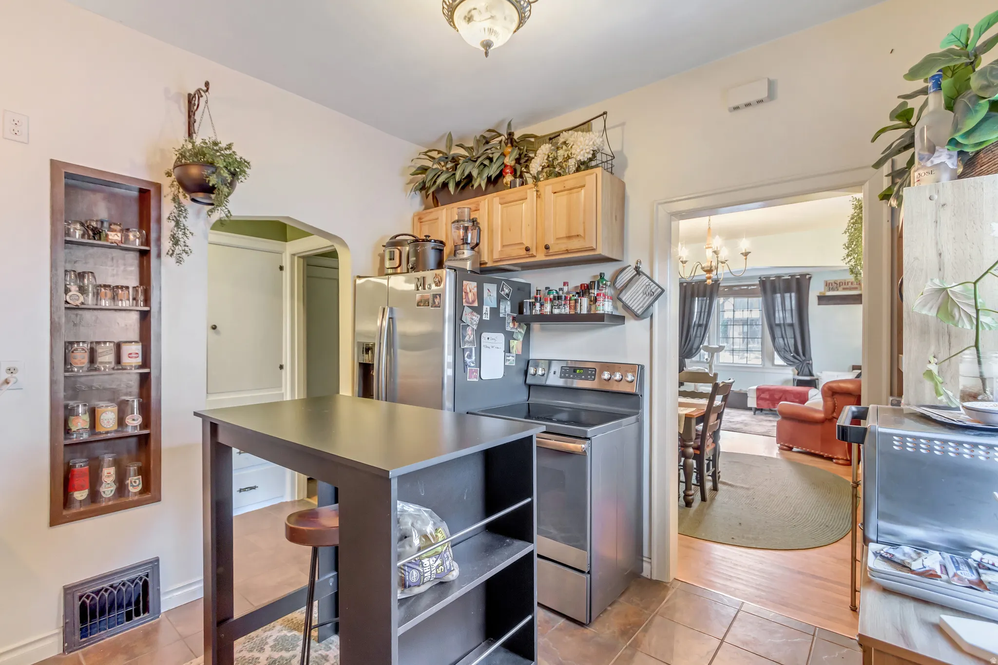 Kitchen featuring arched walkways, stainless steel appliances, light wood finish cabinetry, open shelves, and light tile patterned flooring