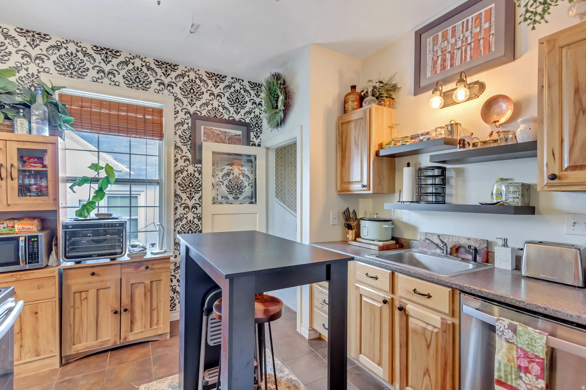 Kitchen with stainless steel appliances, light wood finish cabinets, dark countertops, light tile patterned floors, and glass fronted cabinets