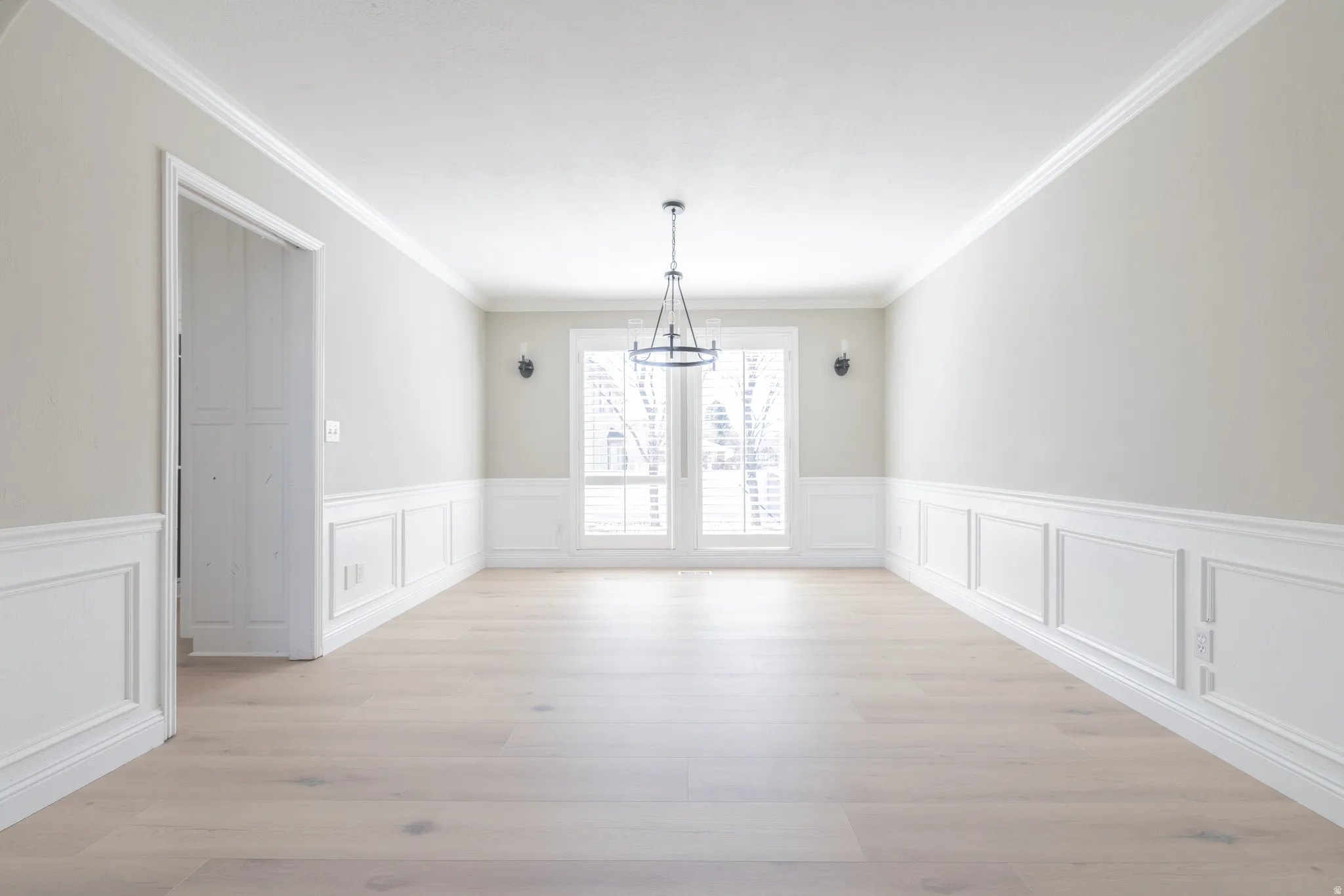 Unfurnished dining area with wainscoting, a decorative wall, crown molding, light wood finished floors, and suspended lighting