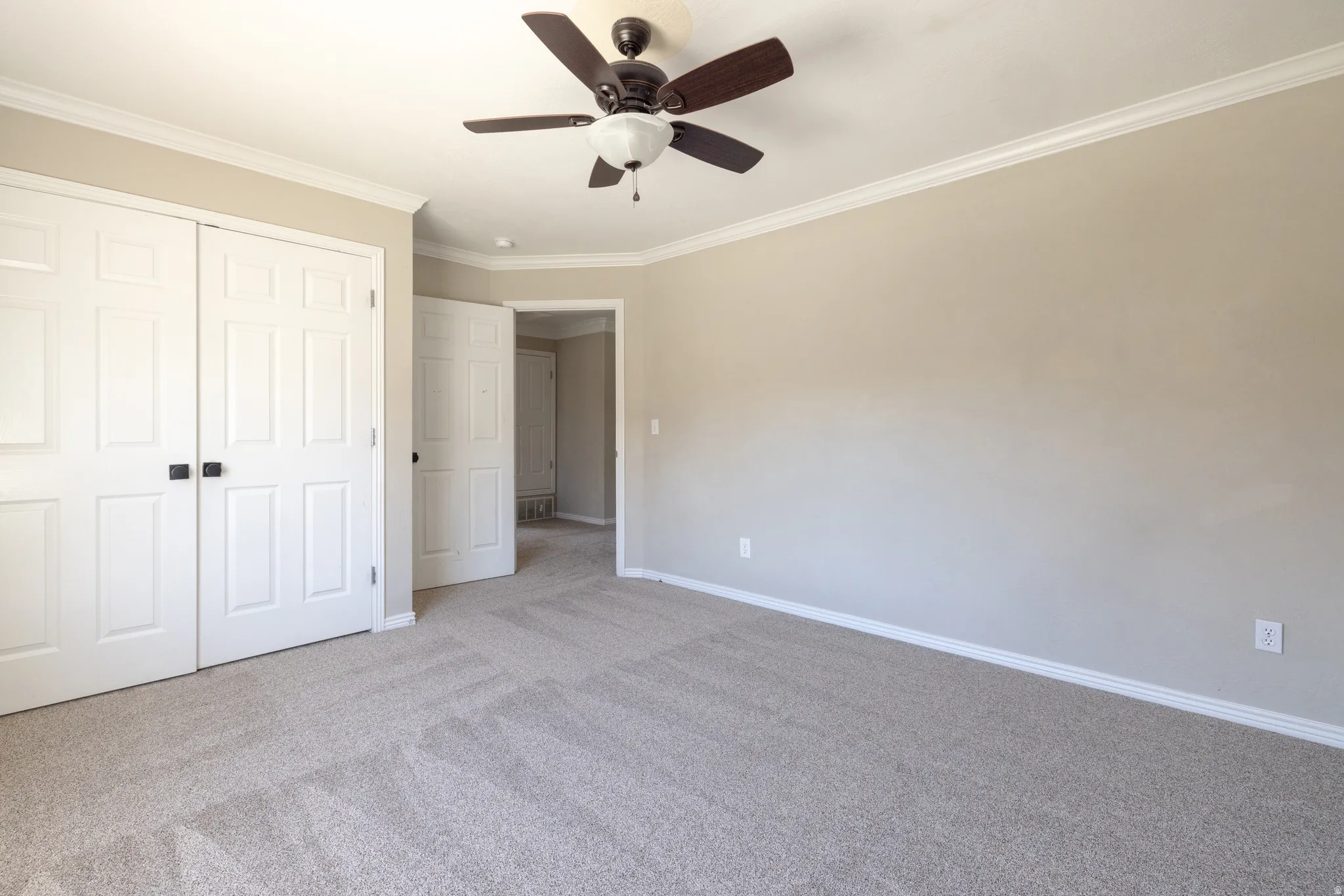 Unfurnished bedroom featuring carpet, crown molding, ceiling fan, and a closet