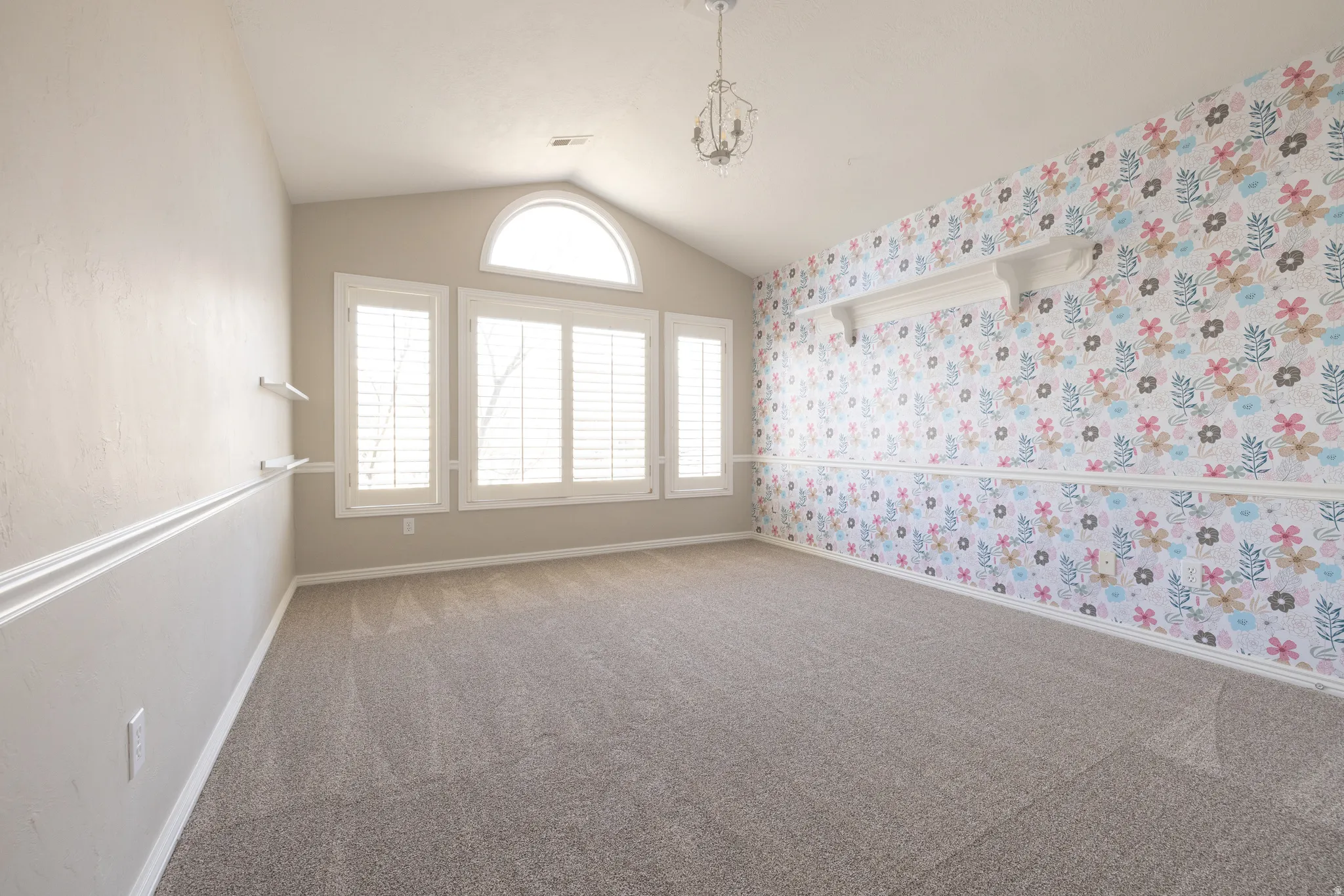 Carpeted spare room with wallpapered walls and a chandelier