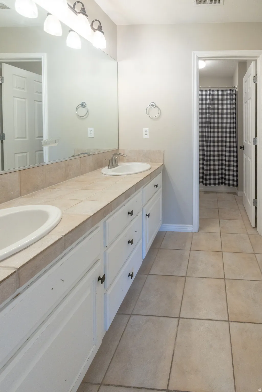 Full bathroom featuring double vanity, a shower with curtain, and light tile patterned floors