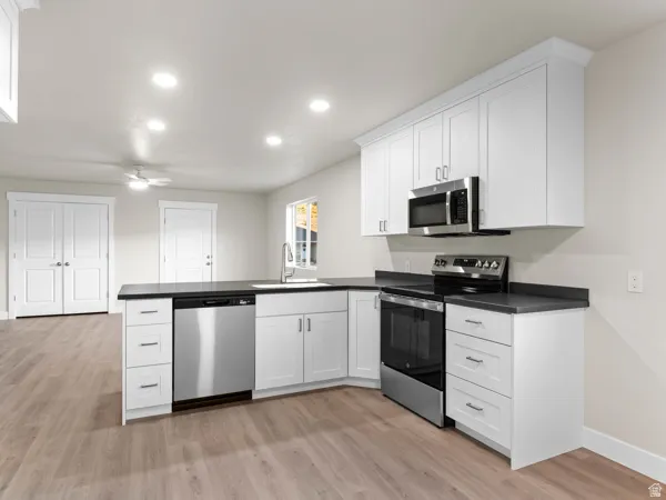 Kitchen featuring stainless steel appliances, dark countertops, white cabinets, a peninsula, and recessed lighting